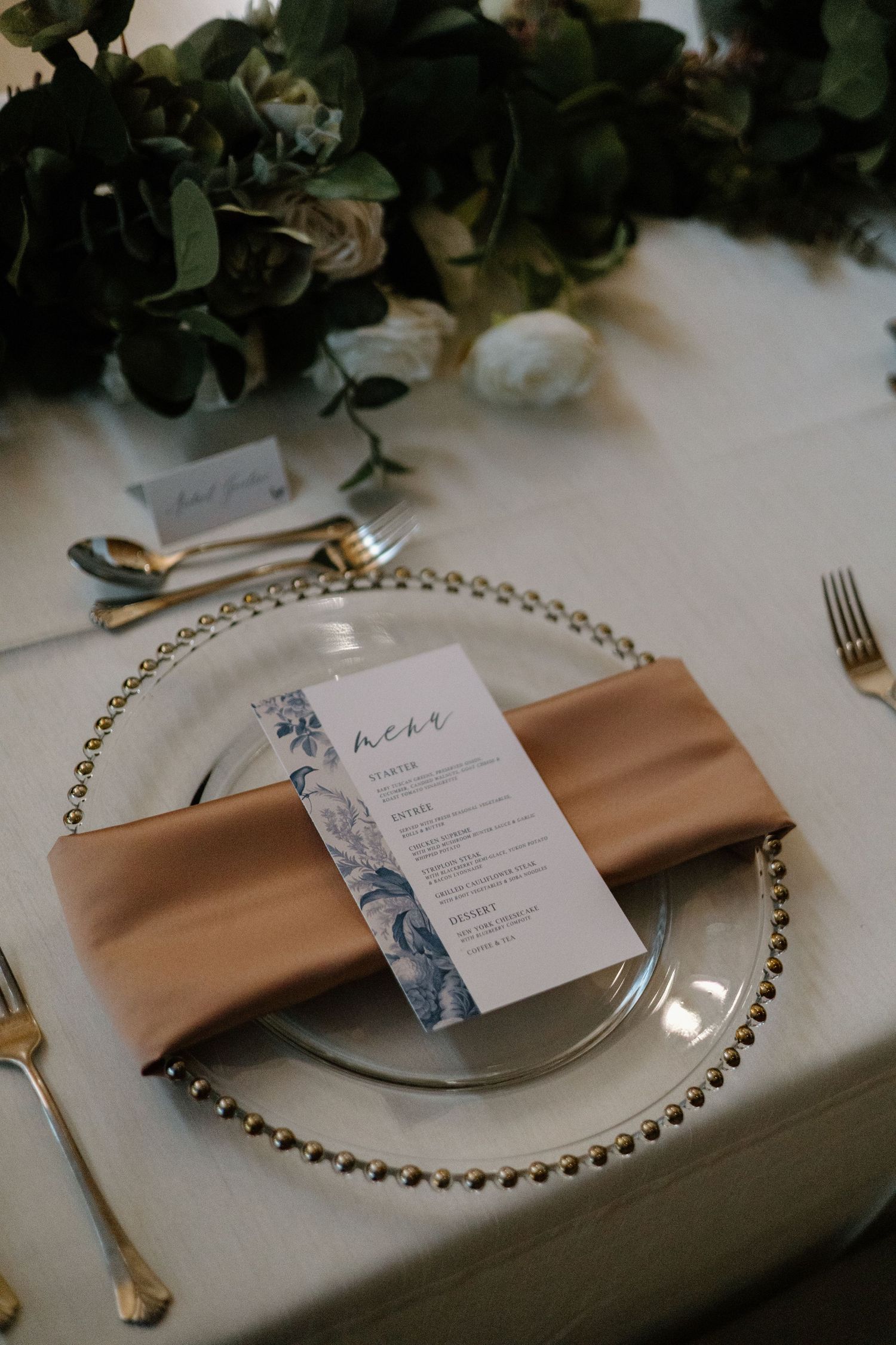Wedding place setting with pearl charger plate, champagne napkin, and floral menu card.