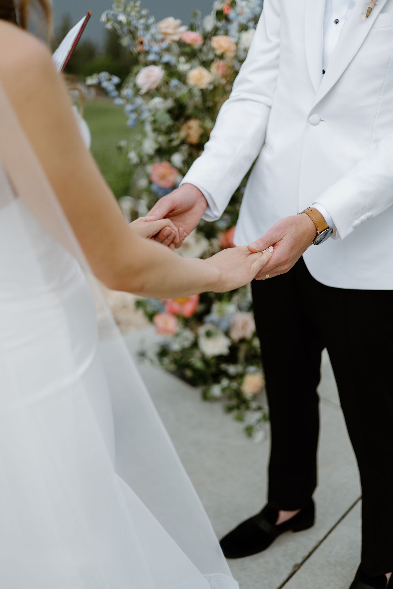 Close-up details of white wedding dress and tuxedo during ceremony.