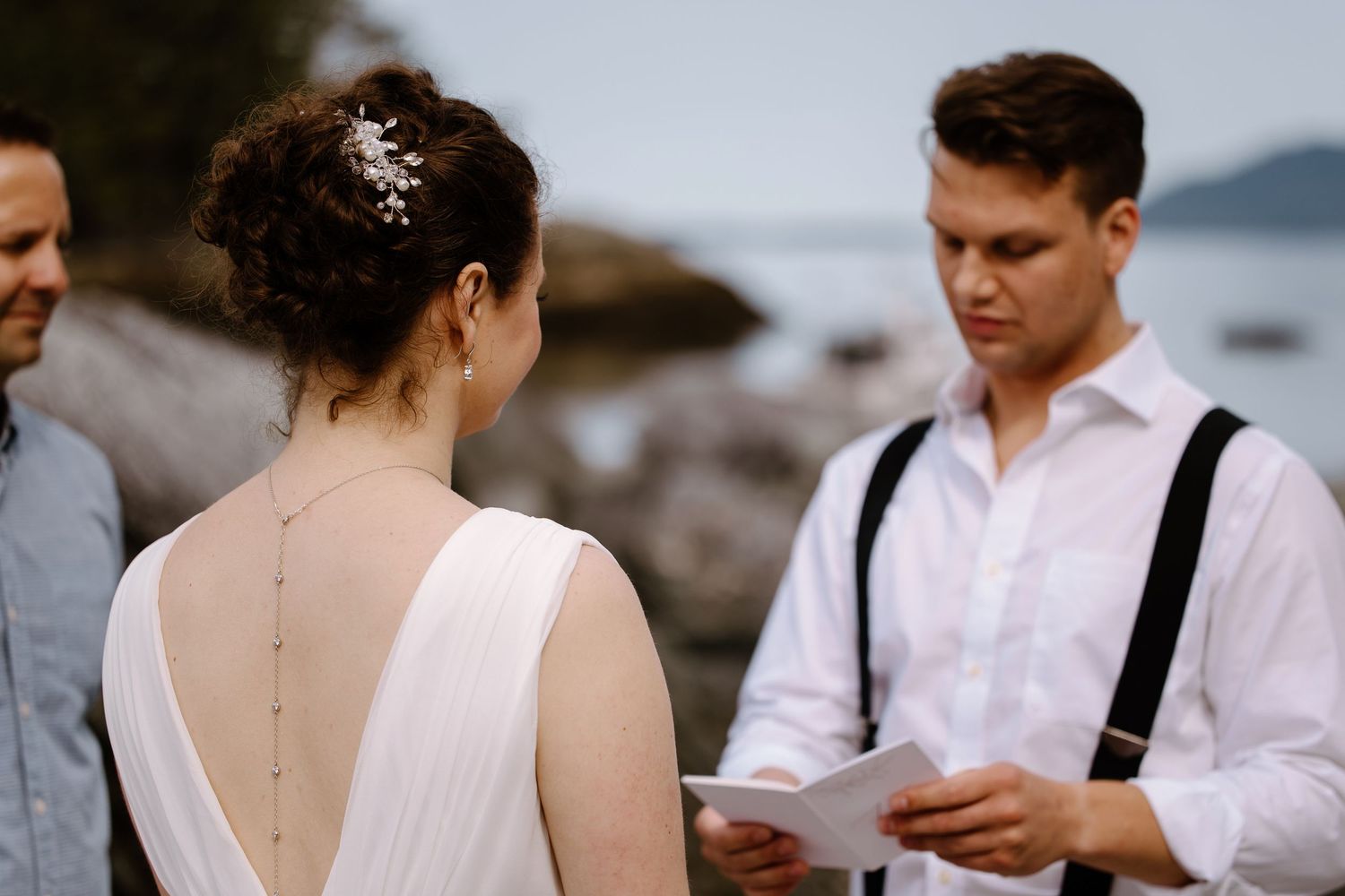 A scenic coastal wedding ceremony with people standing on rocky shoreline overlooking the water.