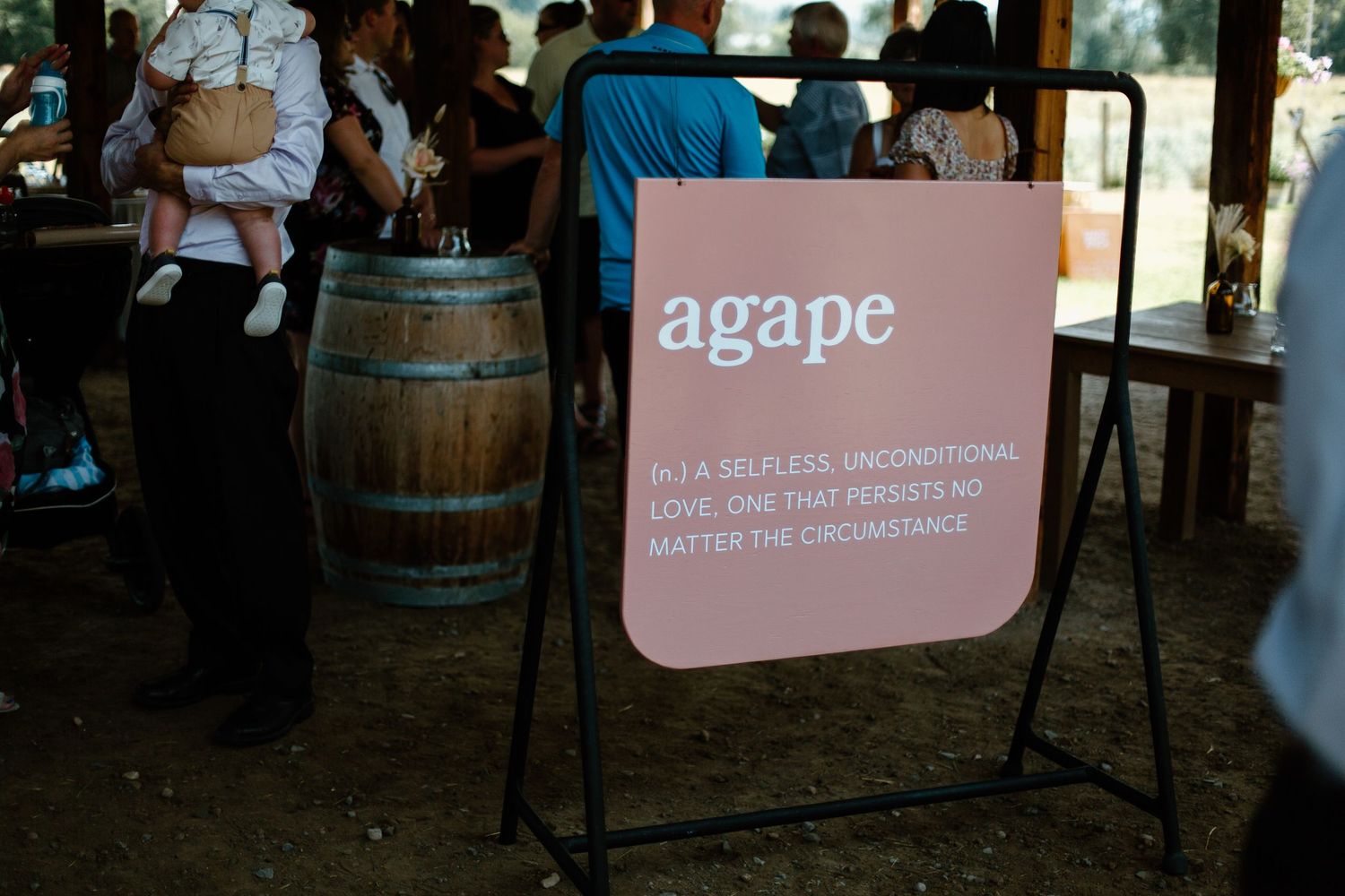 Pink Agape sign displayed at rustic wedding venue with wine barrel in background.