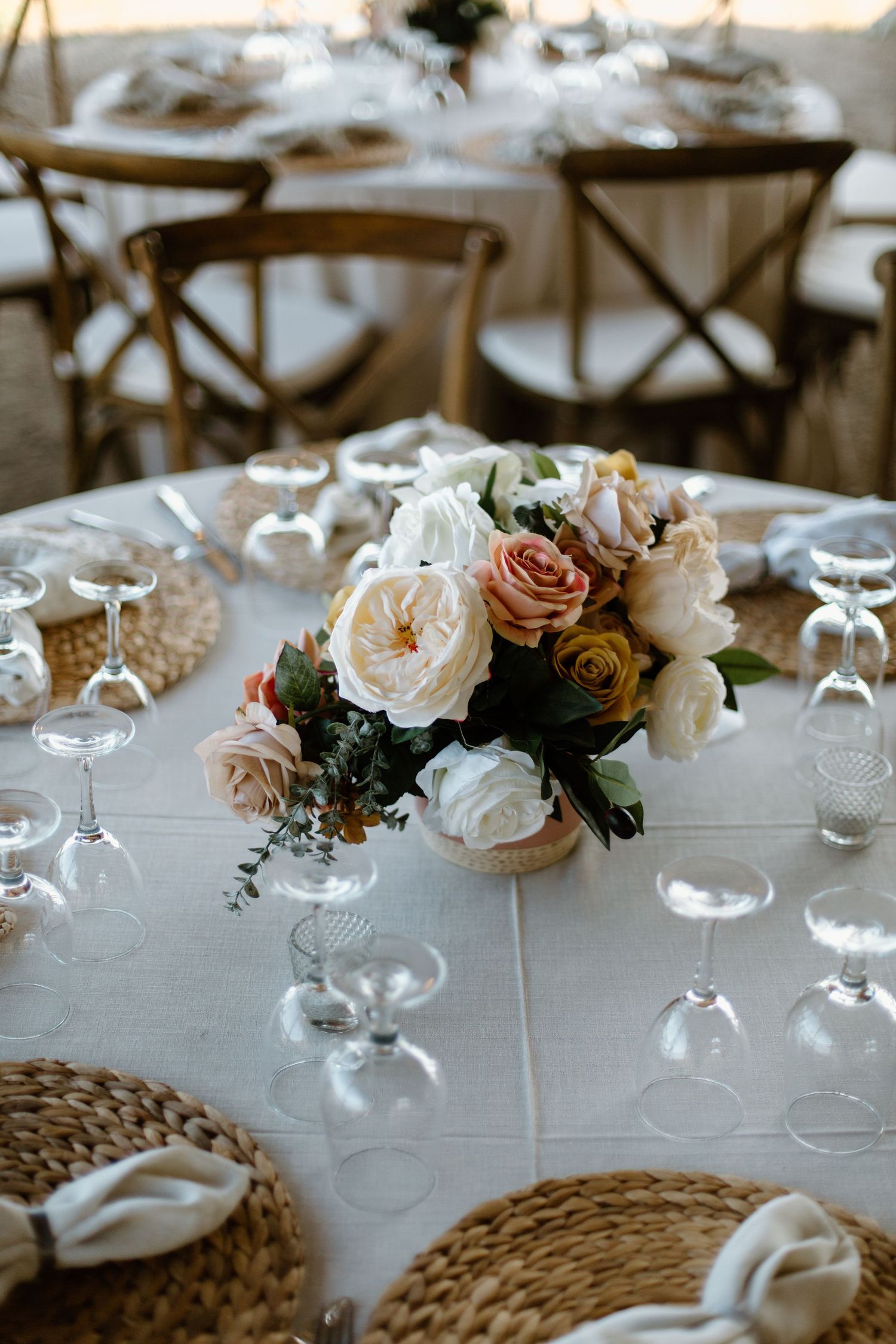 Elegant wedding table centerpiece with blush and white roses surrounded by wine glasses.