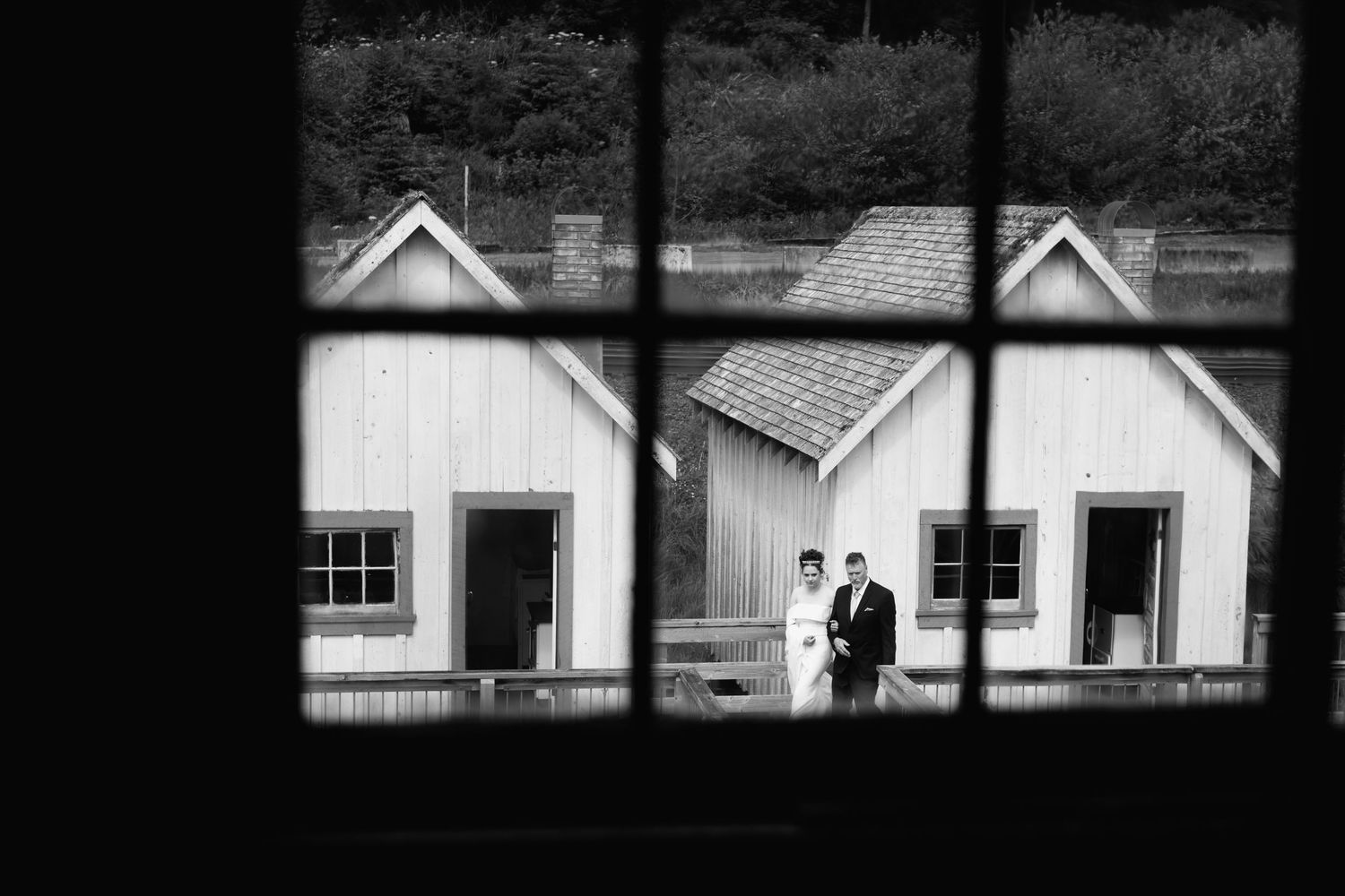 Black and white window view of rustic buildings with couple in distance.