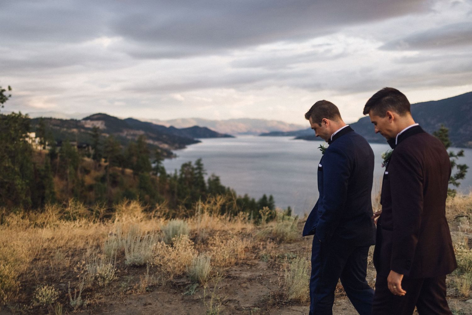 Couple standing on hillside overlooking scenic mountain lake view.