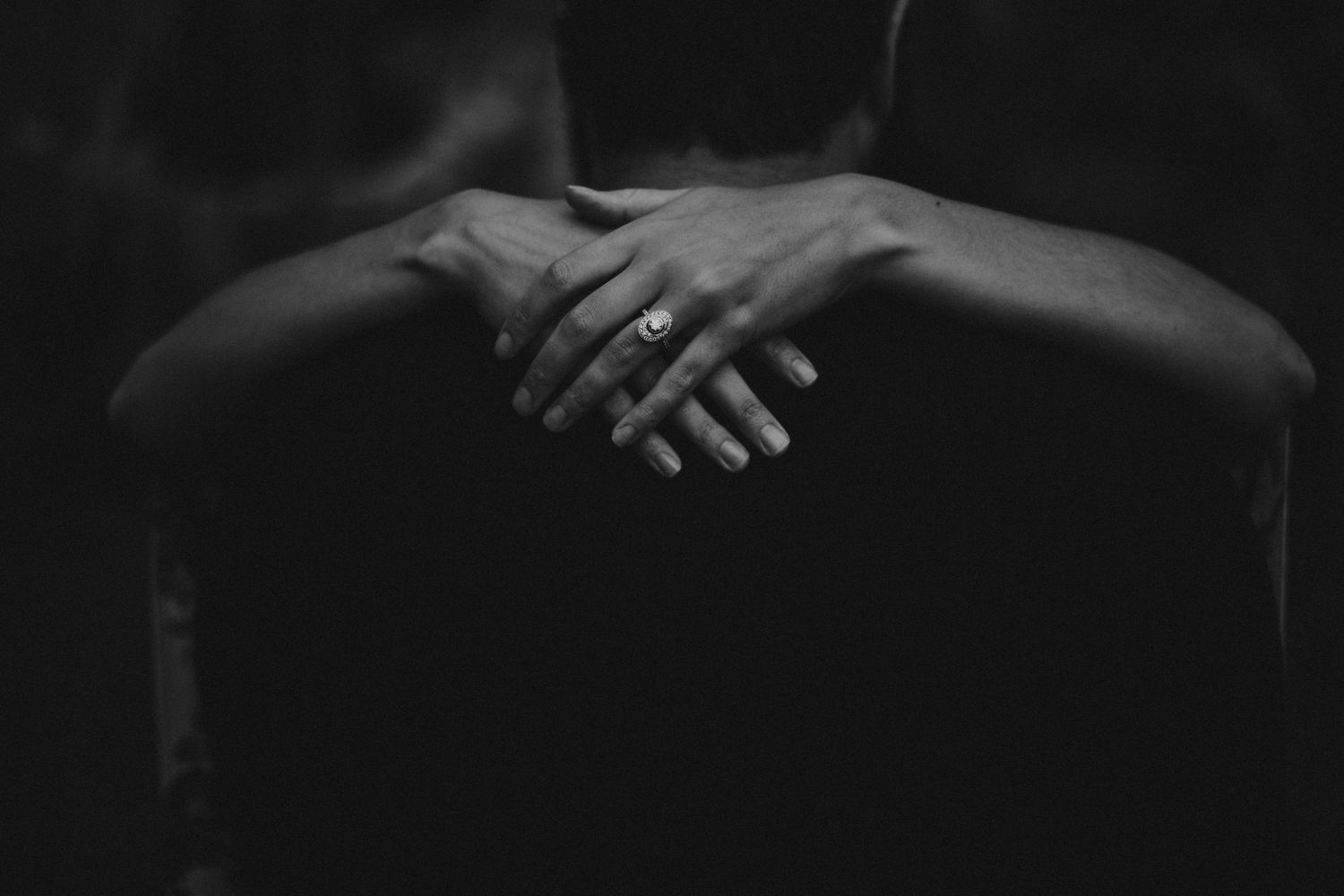 Artistic black and white close-up photograph of hands adorned with rings against a dark background.