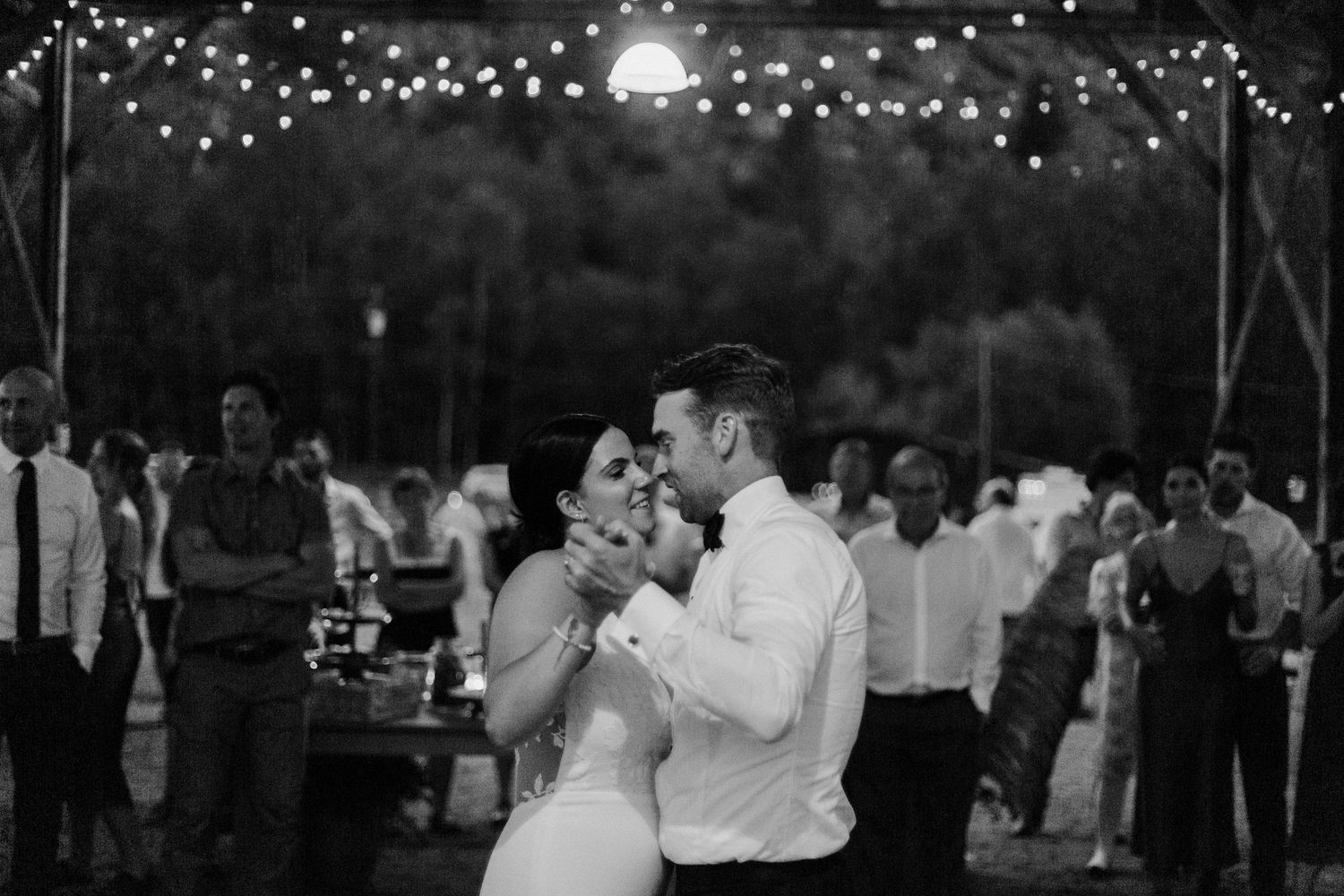 A couple shares their first dance under twinkling lights at their evening wedding reception.