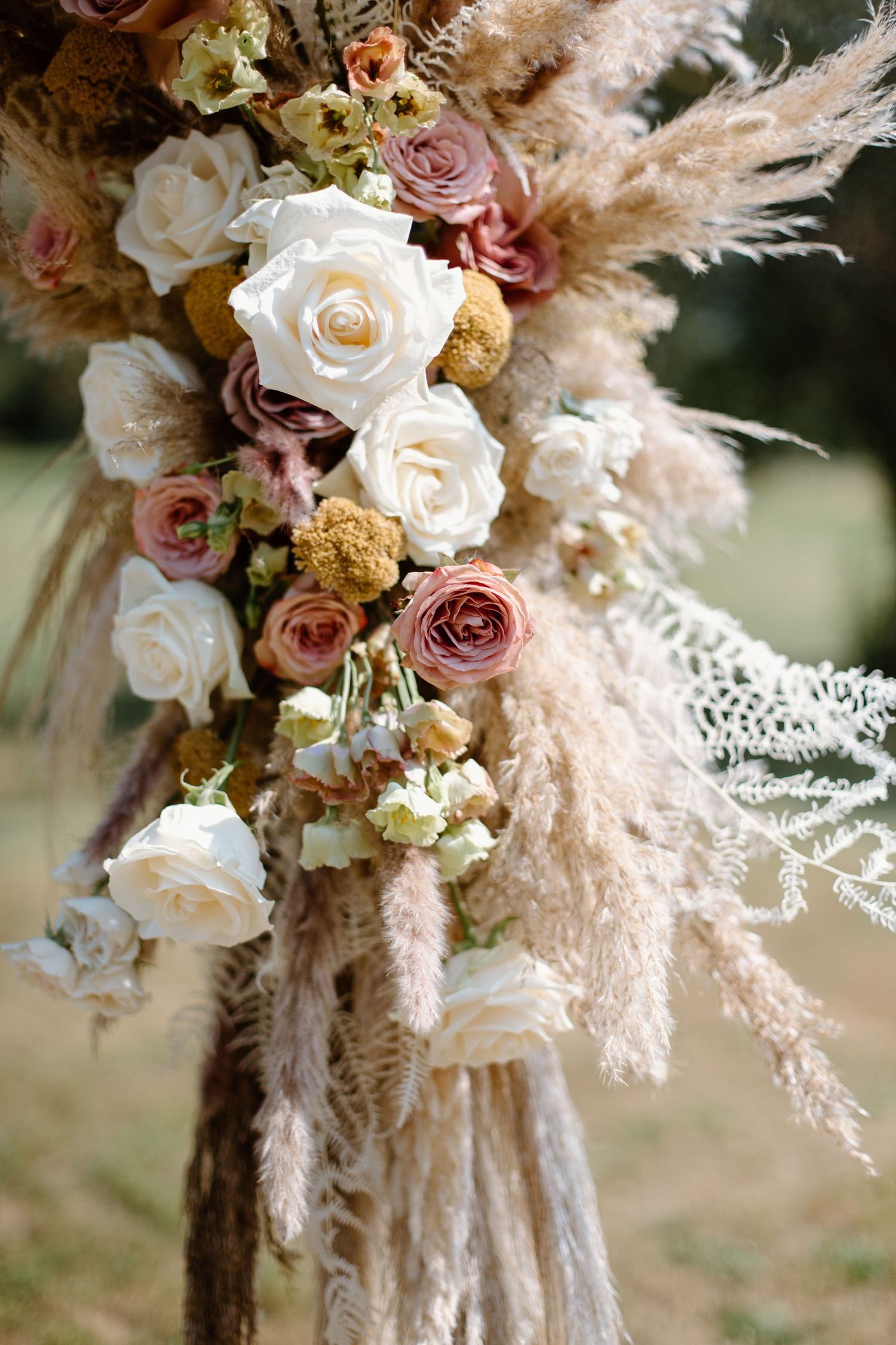 Romantic floral arrangement with soft white roses, pink blooms, and delicate pampas grass in muted earth tones.