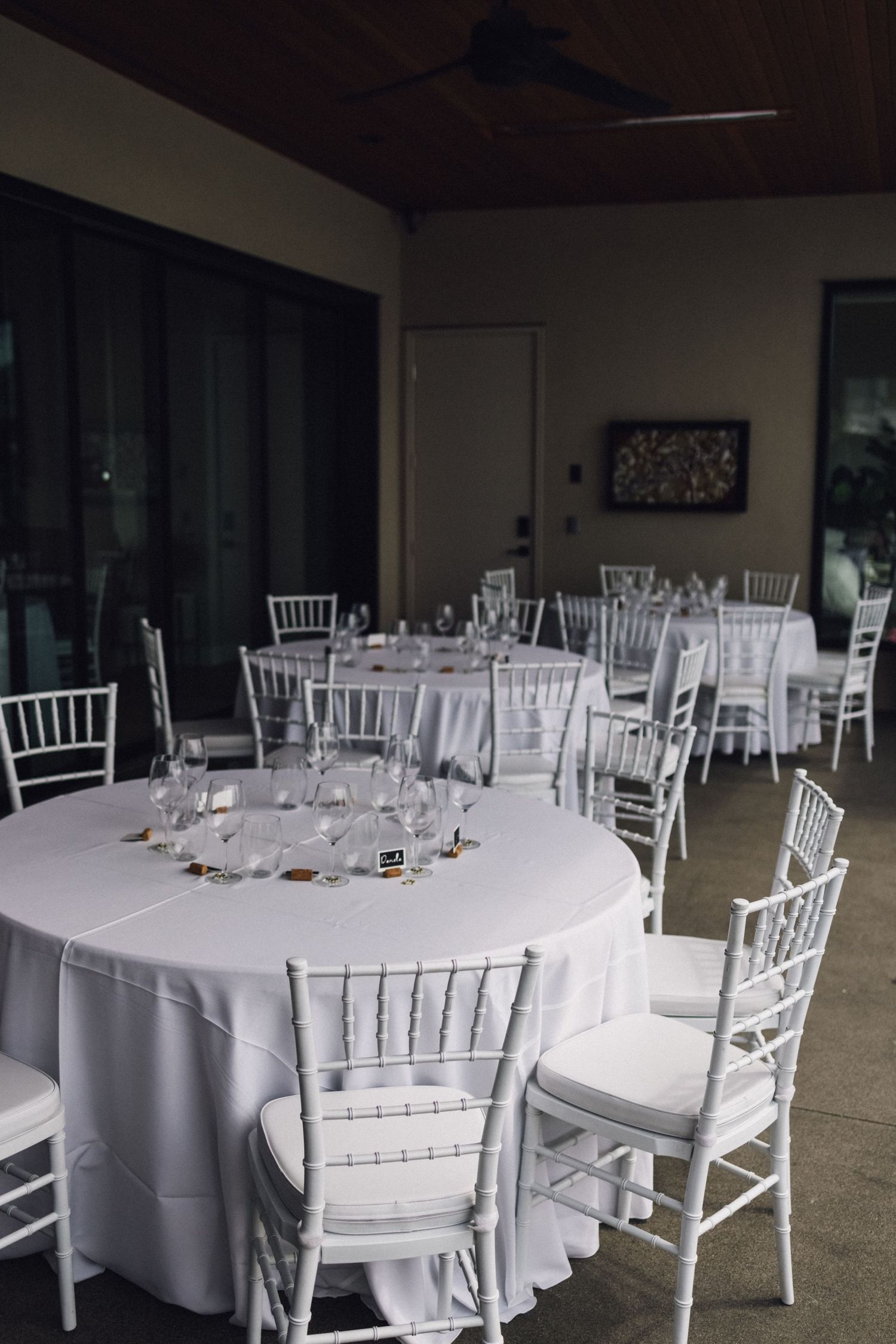 Wedding reception tables set with elegant white chiavari chairs and linens in an indoor venue.