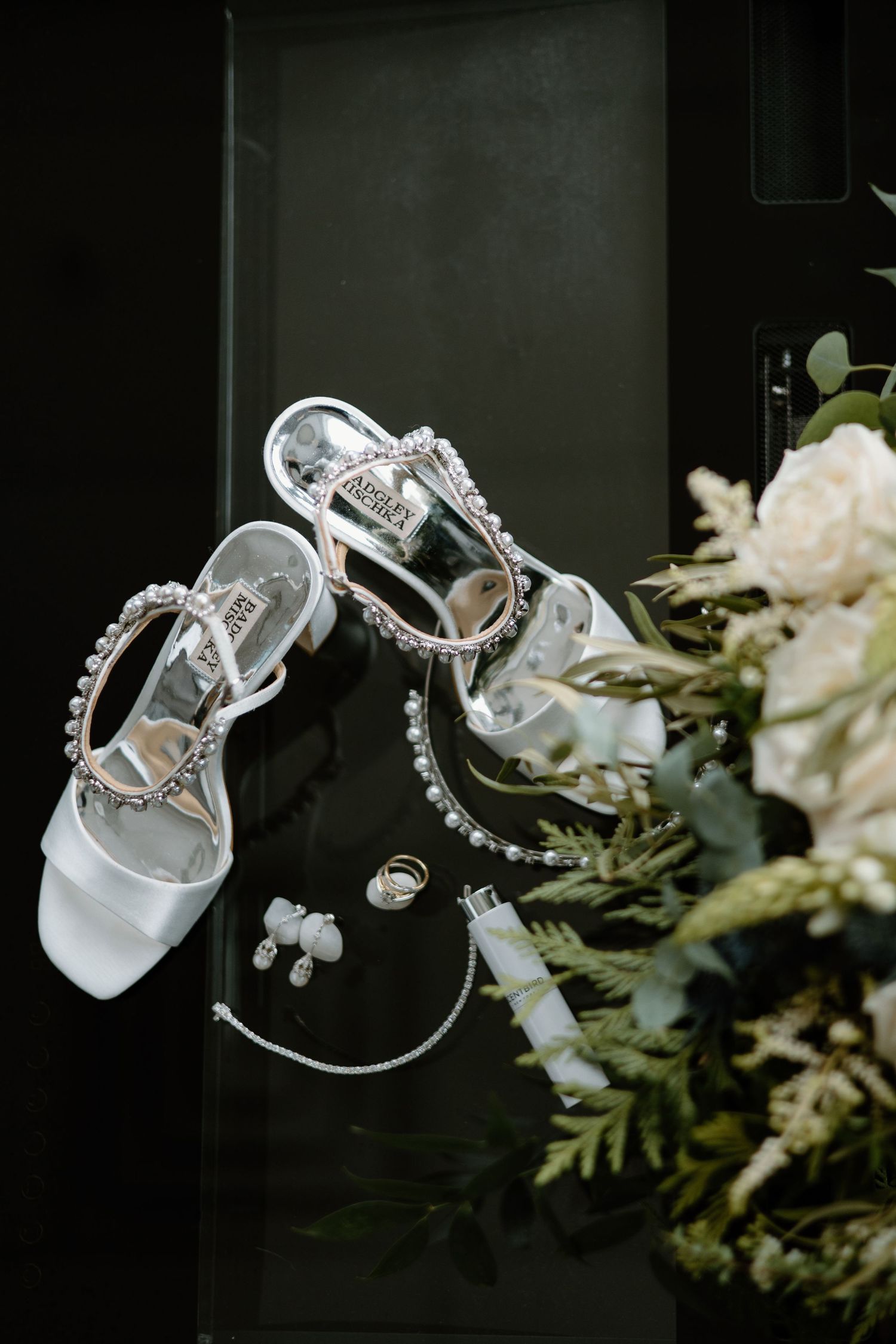 Elegant white bridal shoes with crystal embellishments displayed with white flowers.