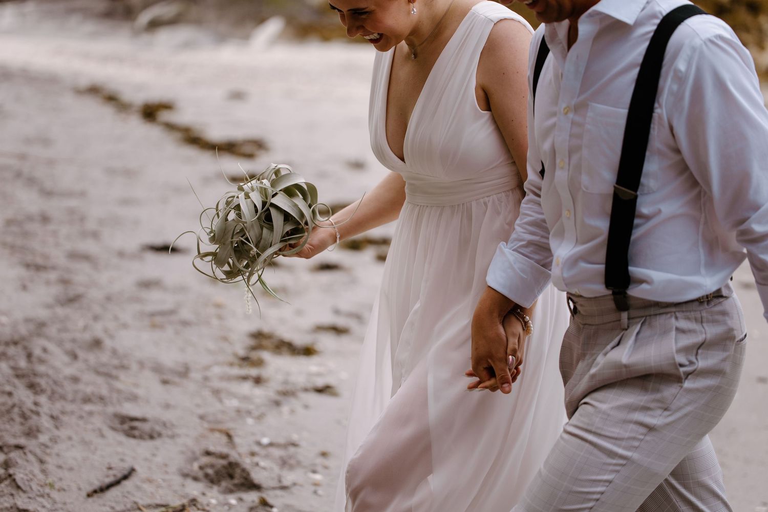 Wedding couple walking hand in hand along a scenic beach shoreline.