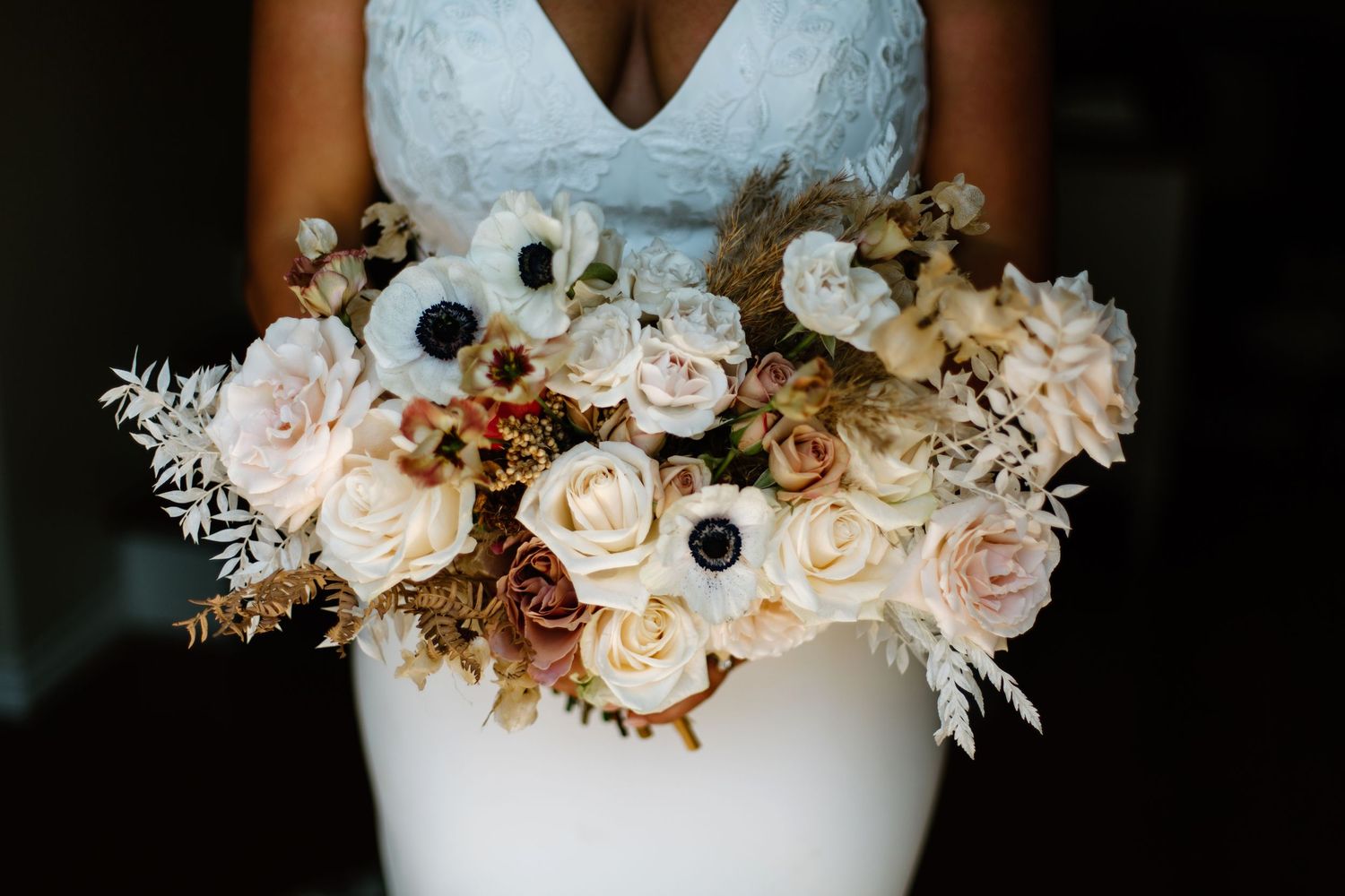 Romantic wedding bouquet with blush roses and anemones against white wedding dress.