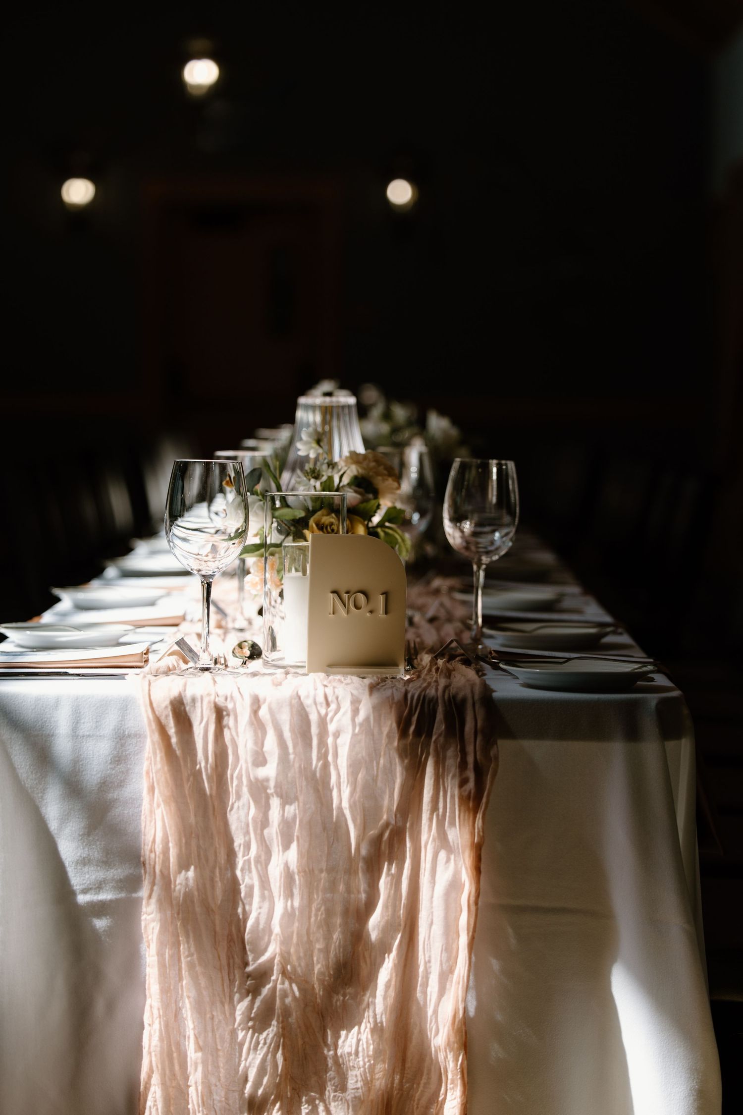 Dramatic lighting illuminates an elegant wedding table setting with blush details and wine glasses.