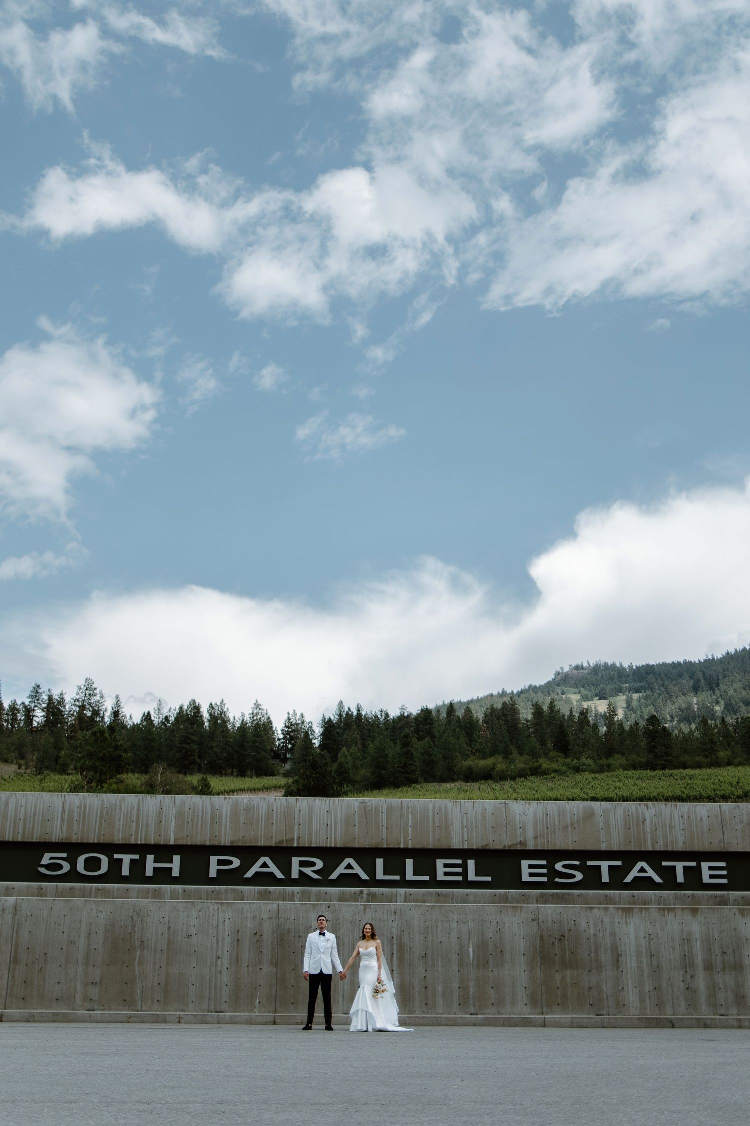 Wedding venue sign for 50th Parallel Estate against a concrete wall with mountain landscape background.