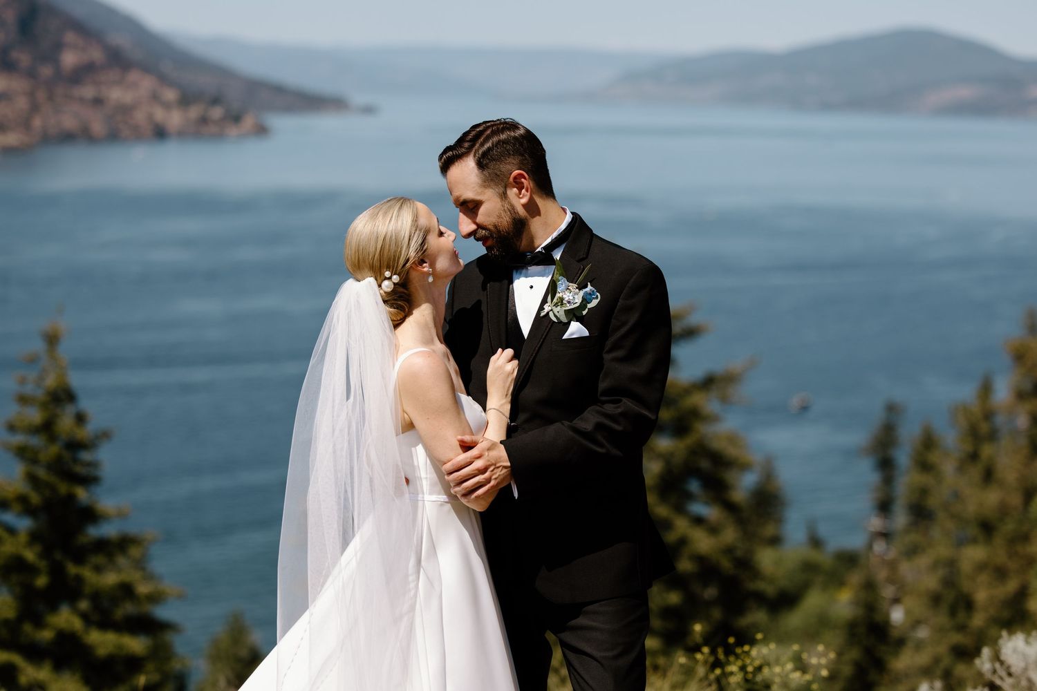 Bride and groom share a romantic moment with a stunning lake and mountain backdrop on their wedding day.