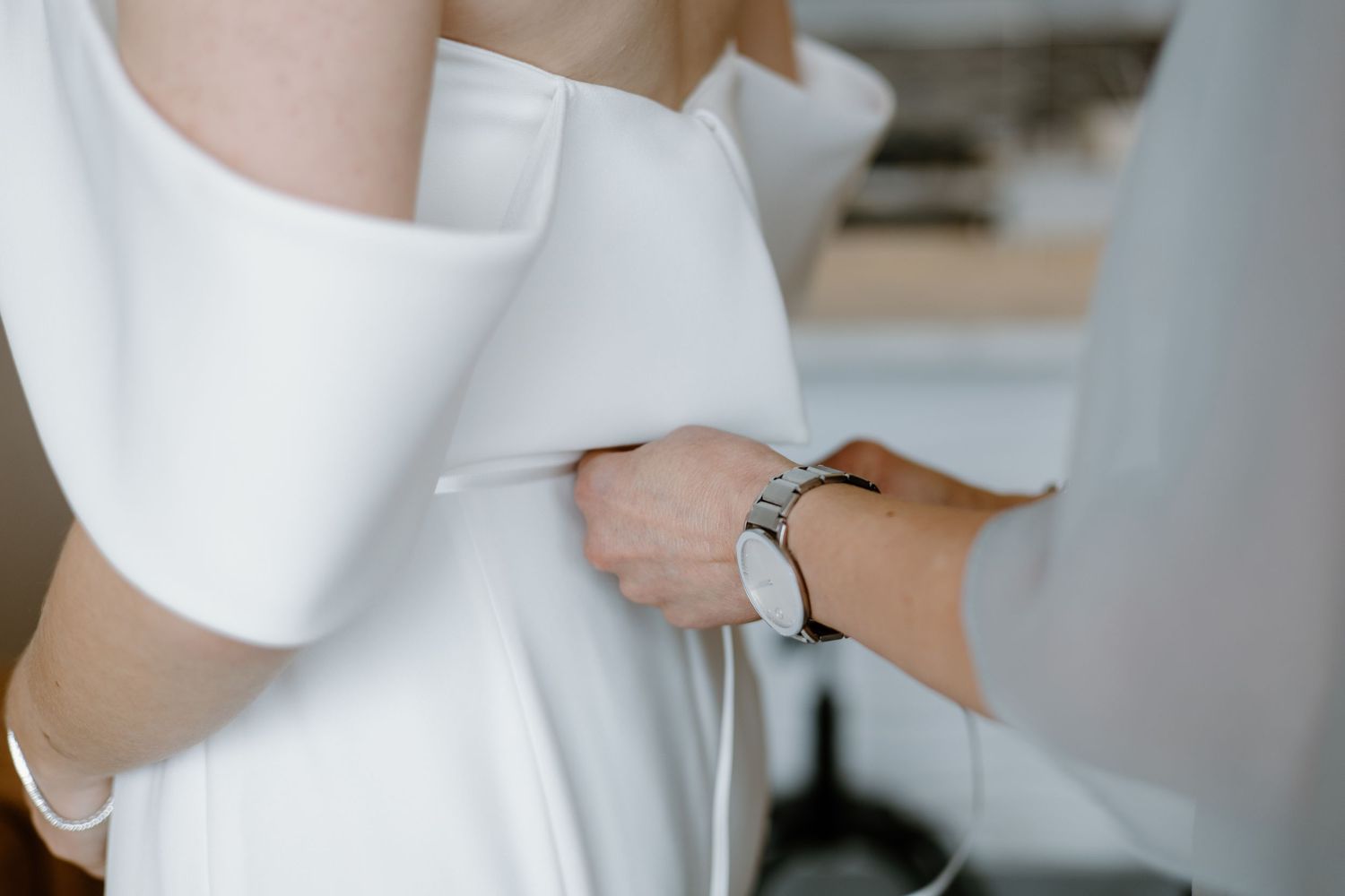 Hands helping to button up a white wedding dress.