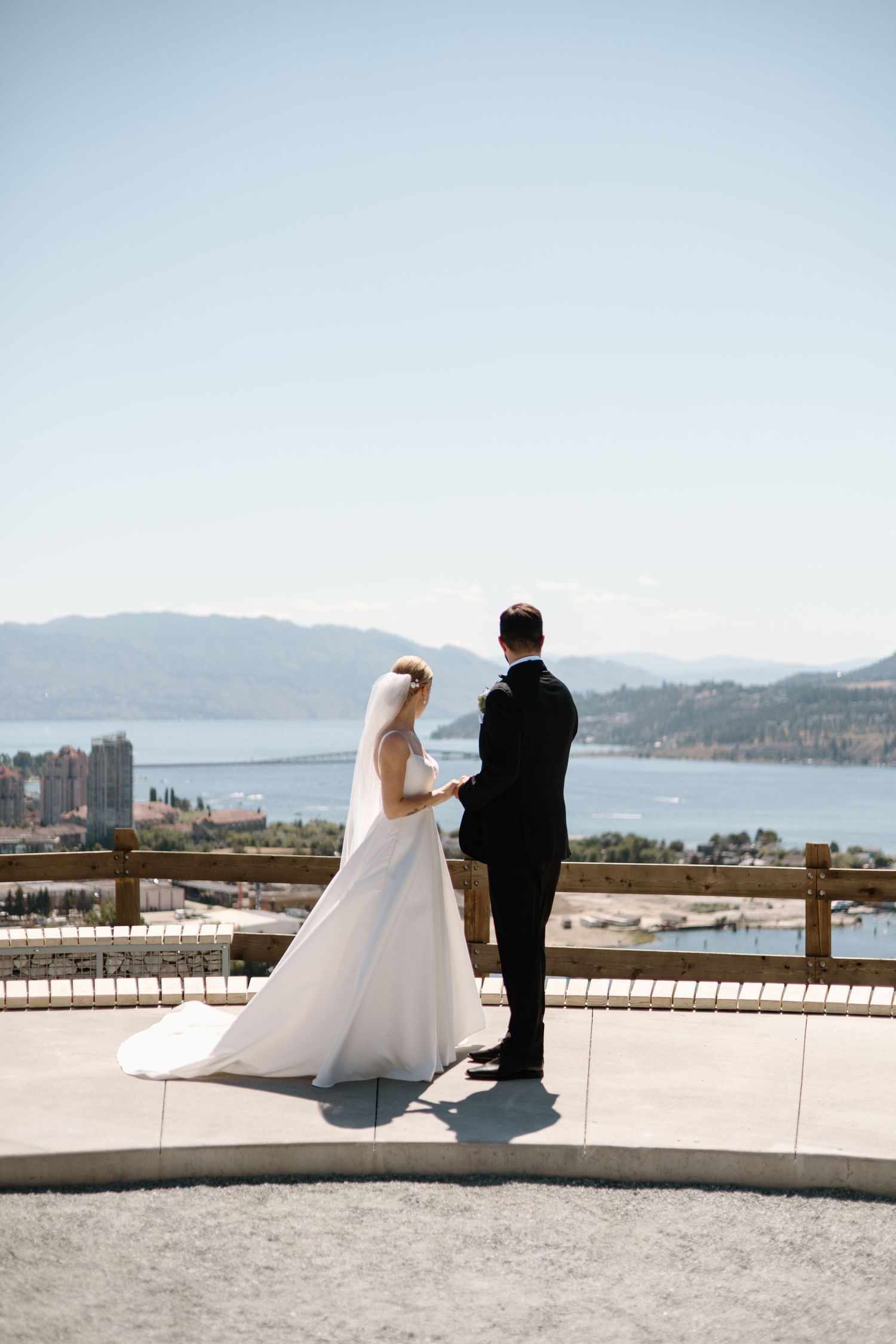 Elegant wedding couple poses at a scenic overlook with mountain and ocean views creating romantic silhouetted photos.