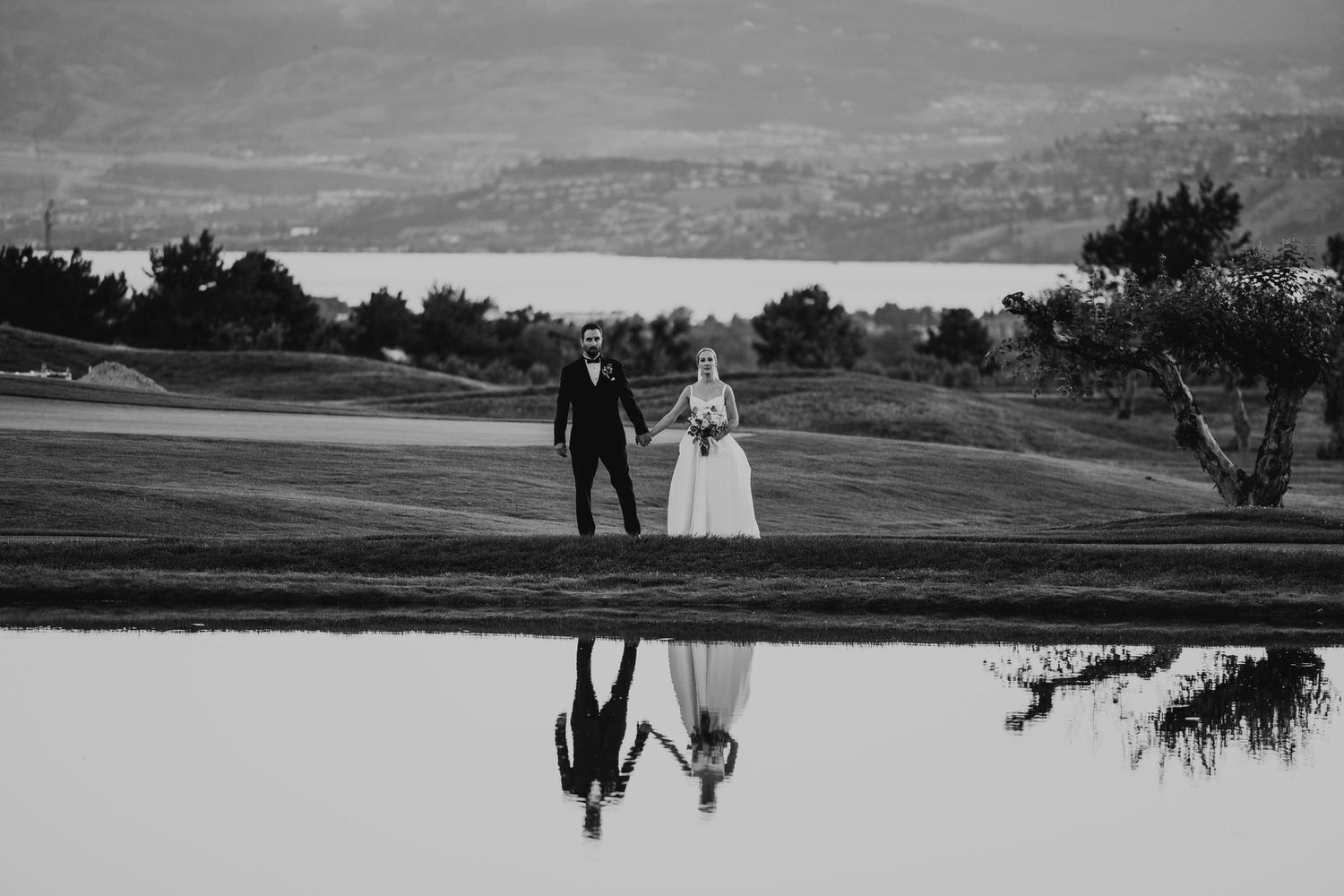 Black and white reflection photo of a couple walking on a golf course with mountains in the background.