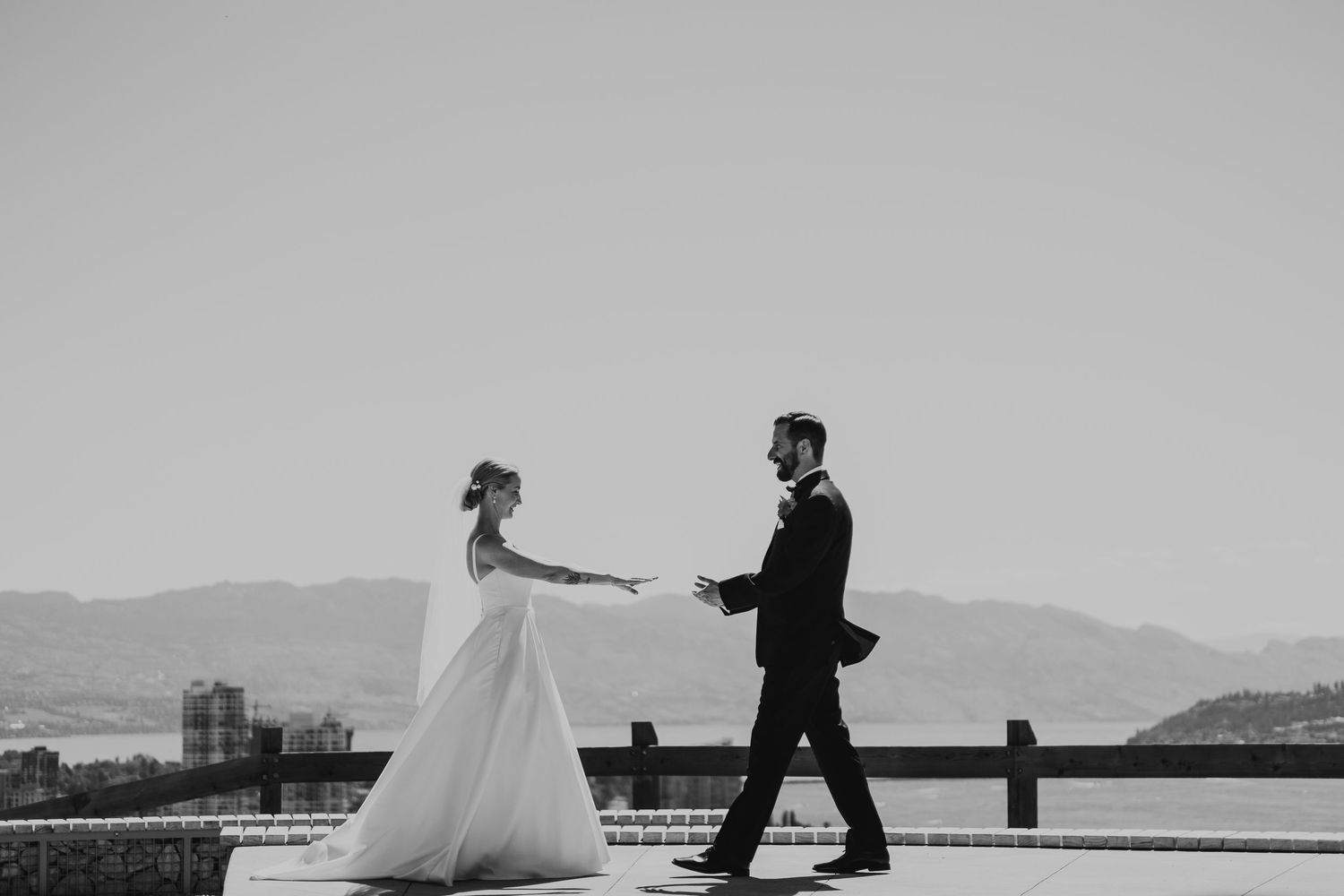 A black and white wedding photo of a couple dancing atop a scenic overlook with mountains in the distance.