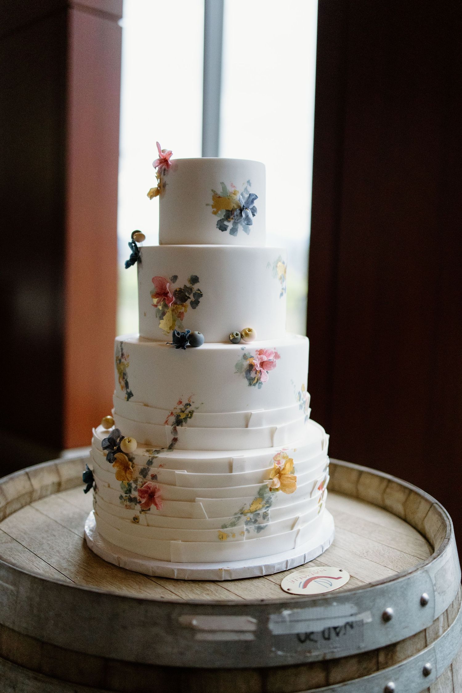 Elegant white wedding cake decorated with delicate floral accents and metallic details on a rustic wooden stand.