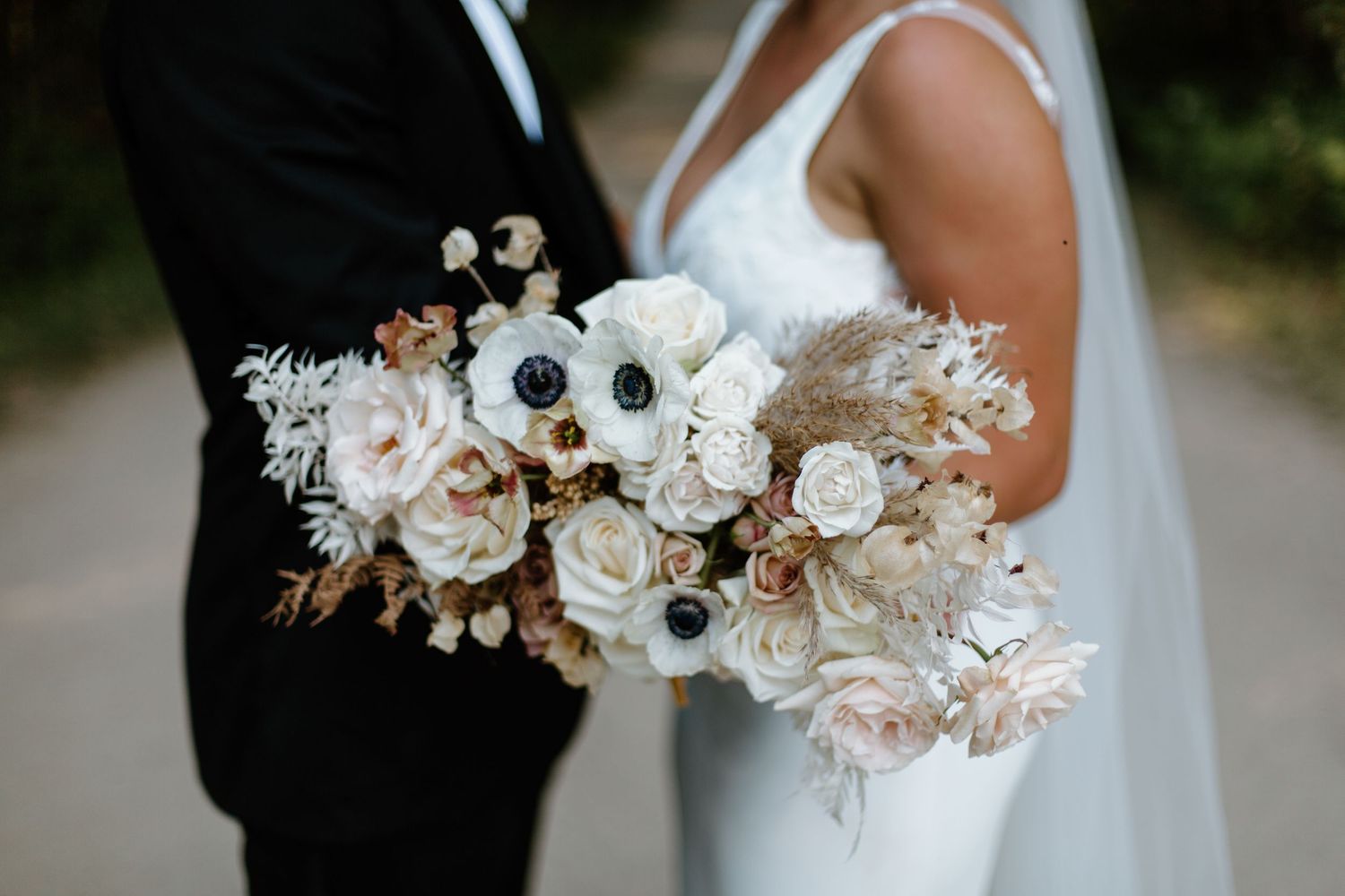A bride and groom stand close together holding a beautiful white and blush floral wedding bouquet.