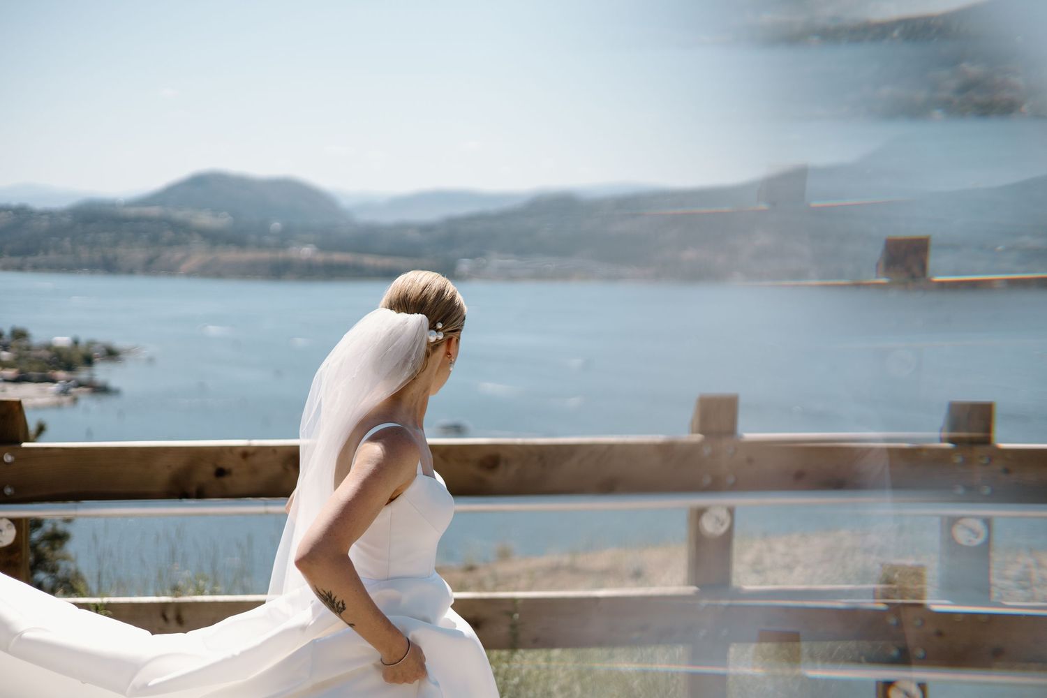 Bride's dress flows in the wind against scenic mountain lake vista.
