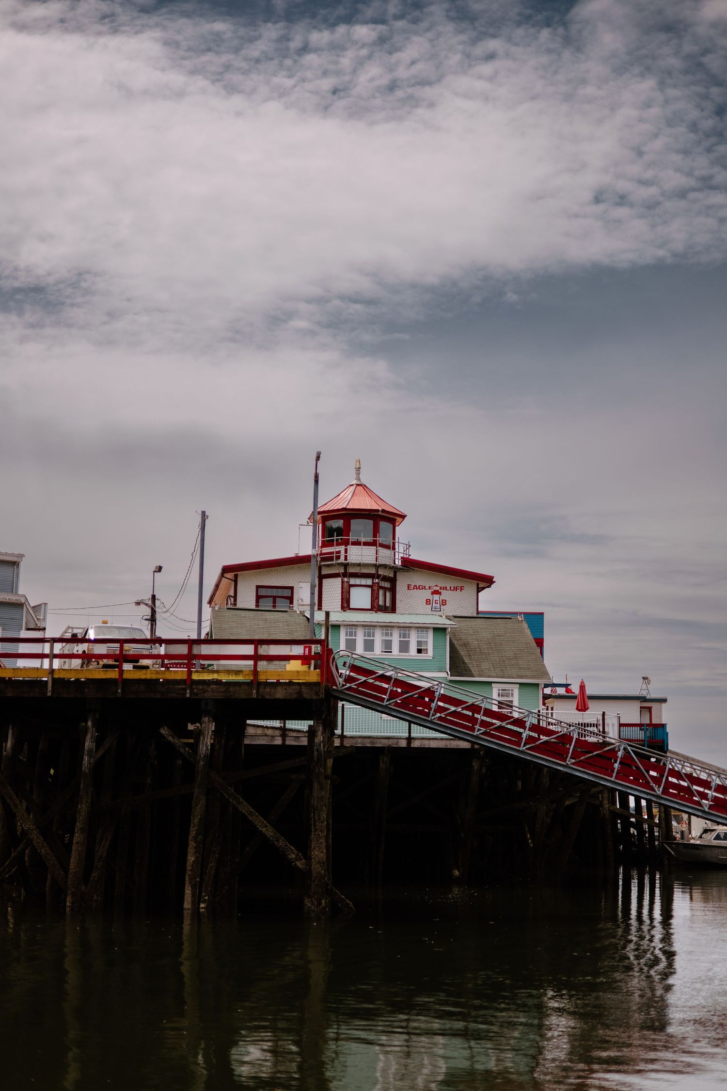 Red-trimmed wooden pier structure extends into water under cloudy skies.