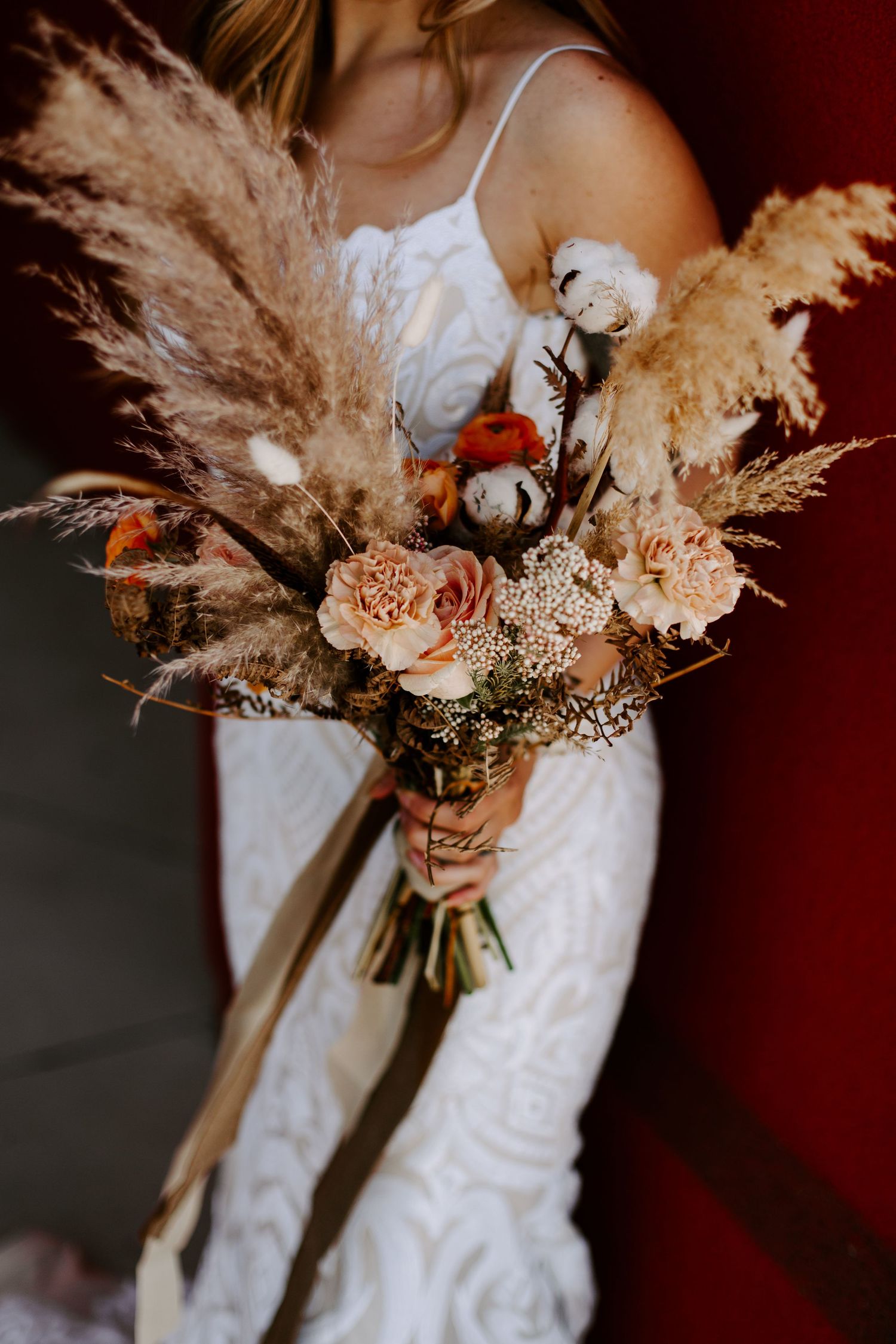 Close up of bohemian wedding bouquet with pampas grass, dried flowers and roses in muted earth tones.