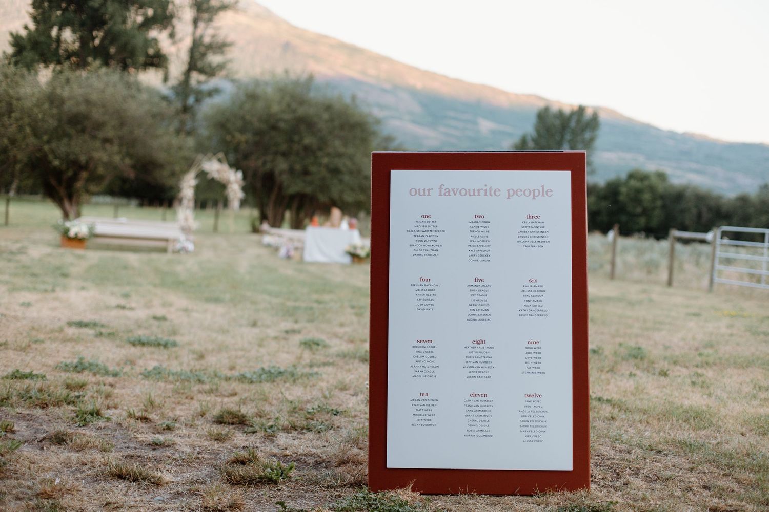 A framed burgundy seating chart displayed outdoors with mountains in the background.