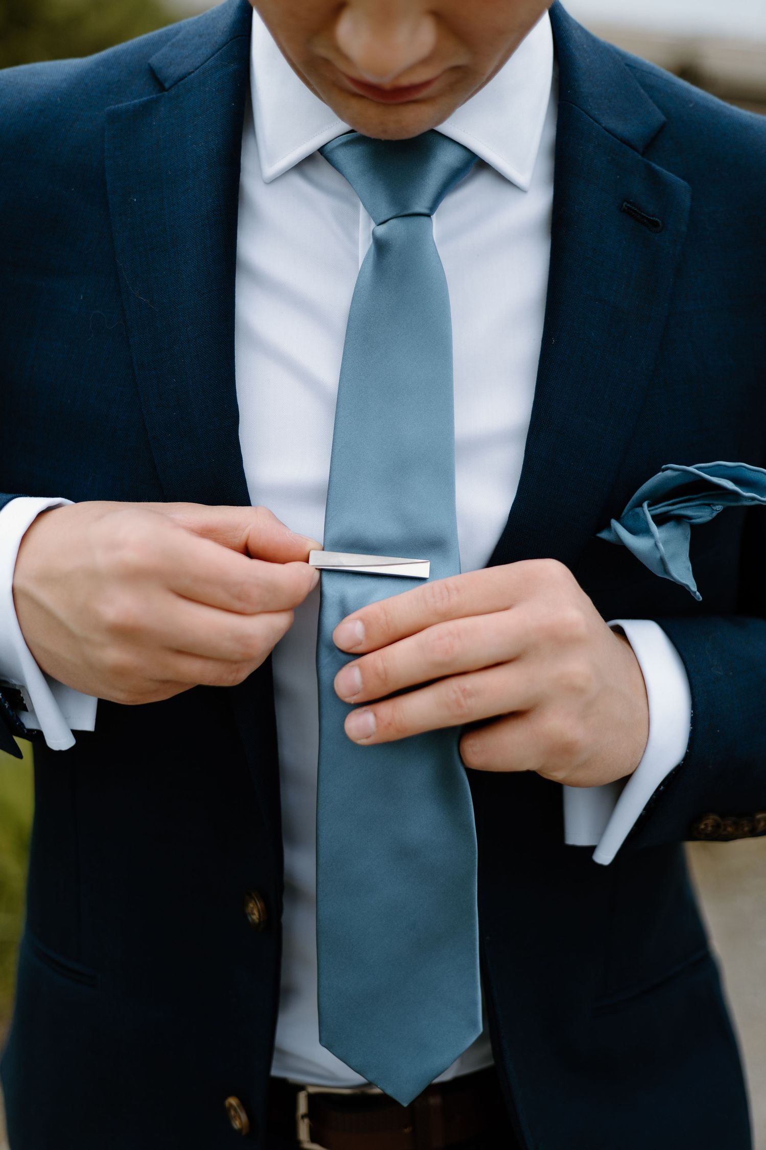 Close-up of hands adjusting a light blue tie against a navy suit jacket.