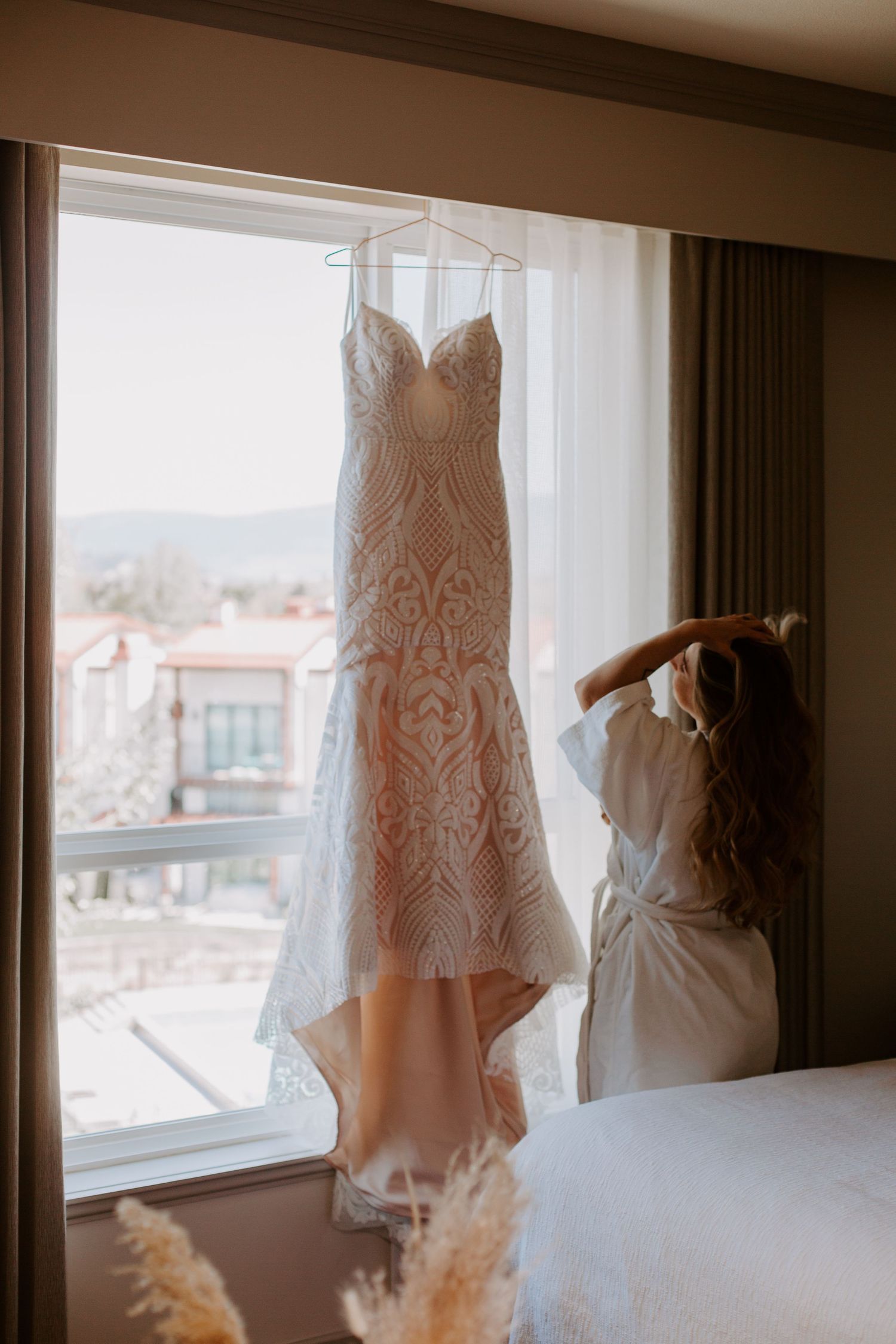 Lace wedding dress hanging in window with mountain view.