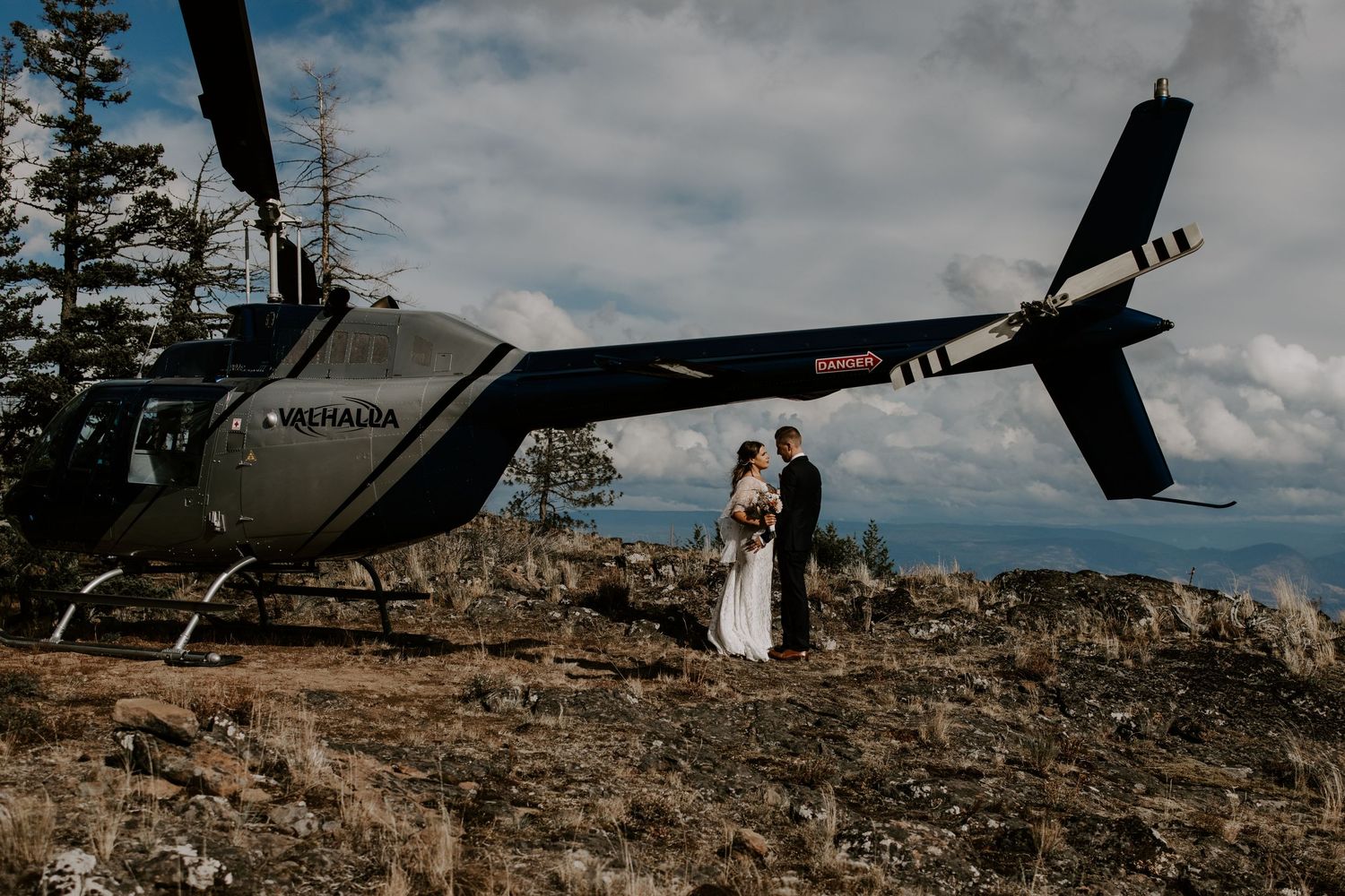 A black helicopter parked on a rocky mountain peak during an outdoor wedding ceremony.