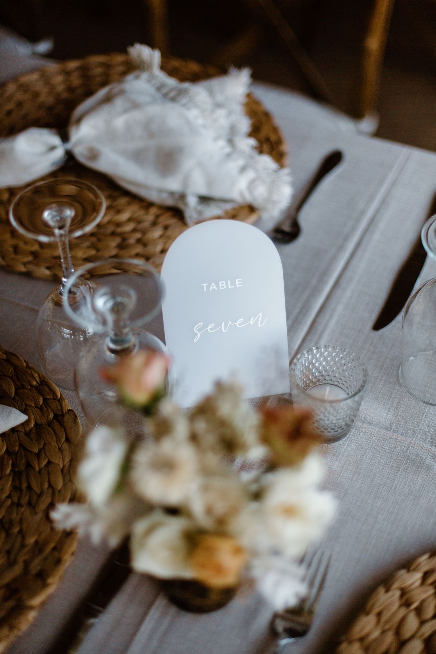Wedding table place setting with woven charger, wine glasses and elegant table number.