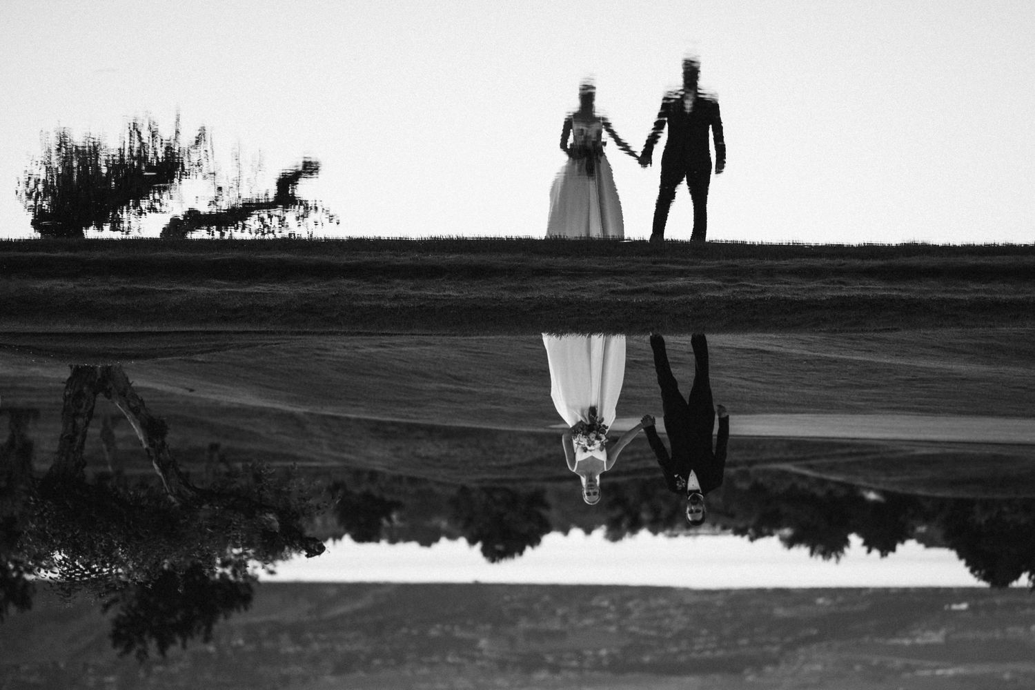 Wedding couple silhouettes stand on a hilltop against a white sky at sunset.