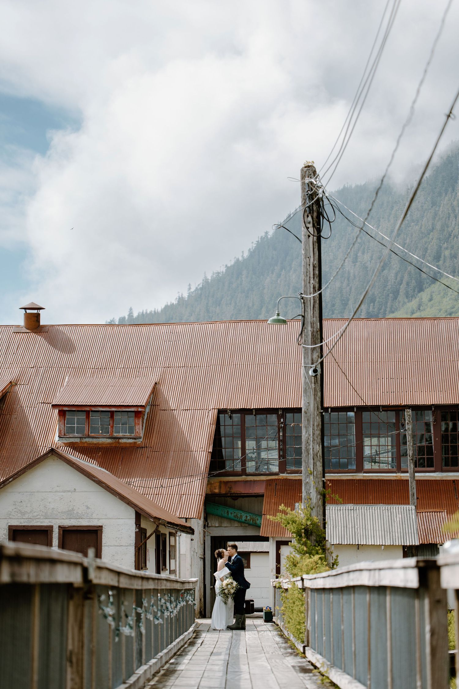 Rows of abandoned wooden buildings with metal roofs line a walkway in a remote mountainous area.