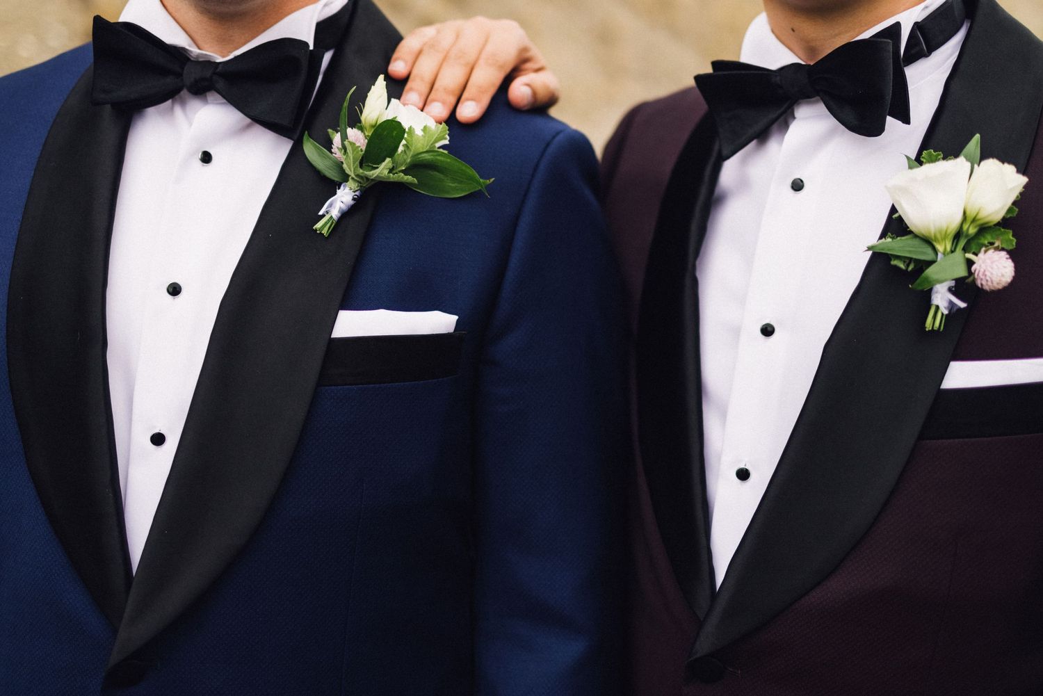 A row of groomsmen in black tuxedos with white boutonnieres stand together at a formal wedding event.