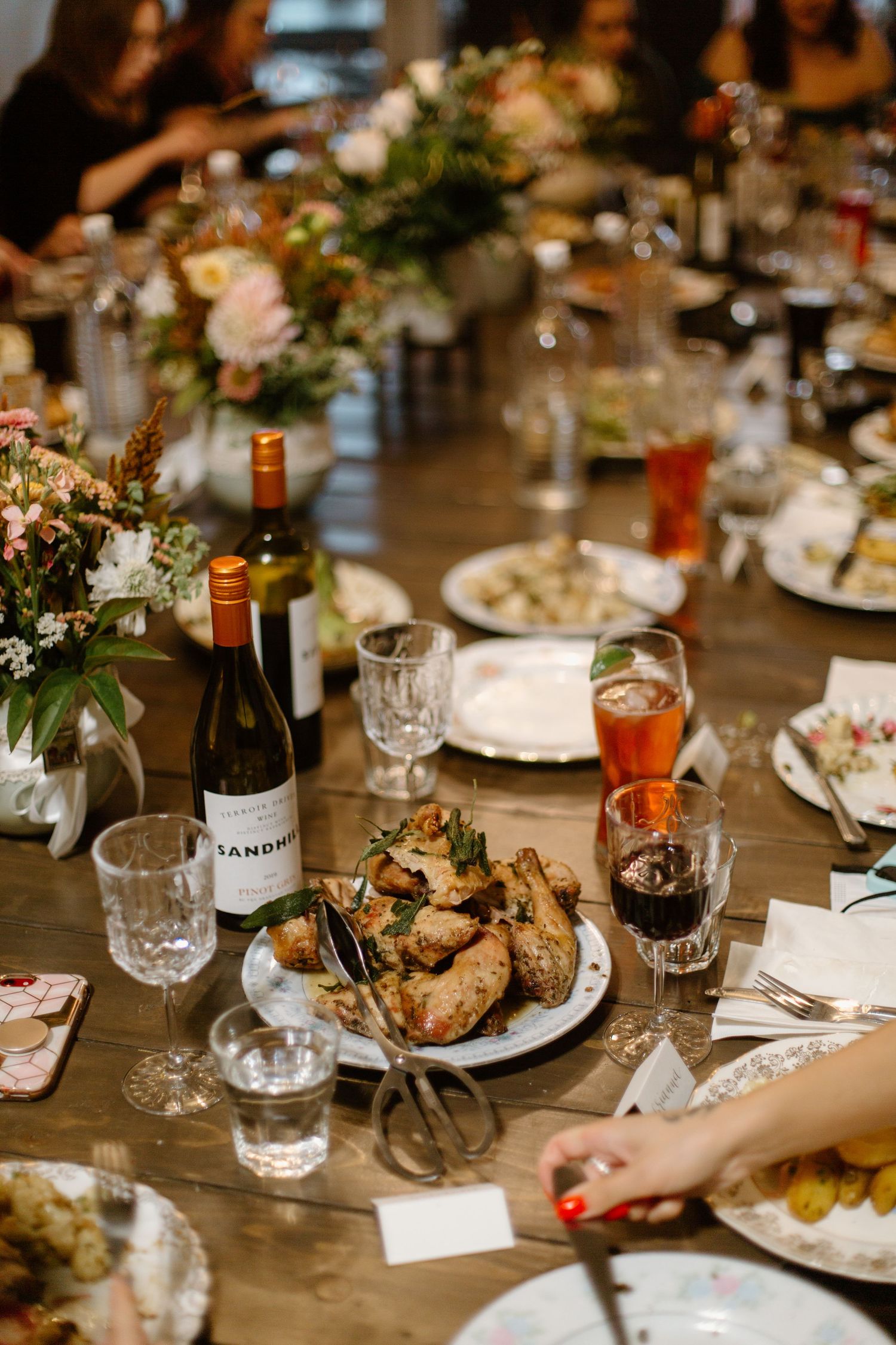 Wedding reception table with wine bottles, floral arrangements, and plates of food.