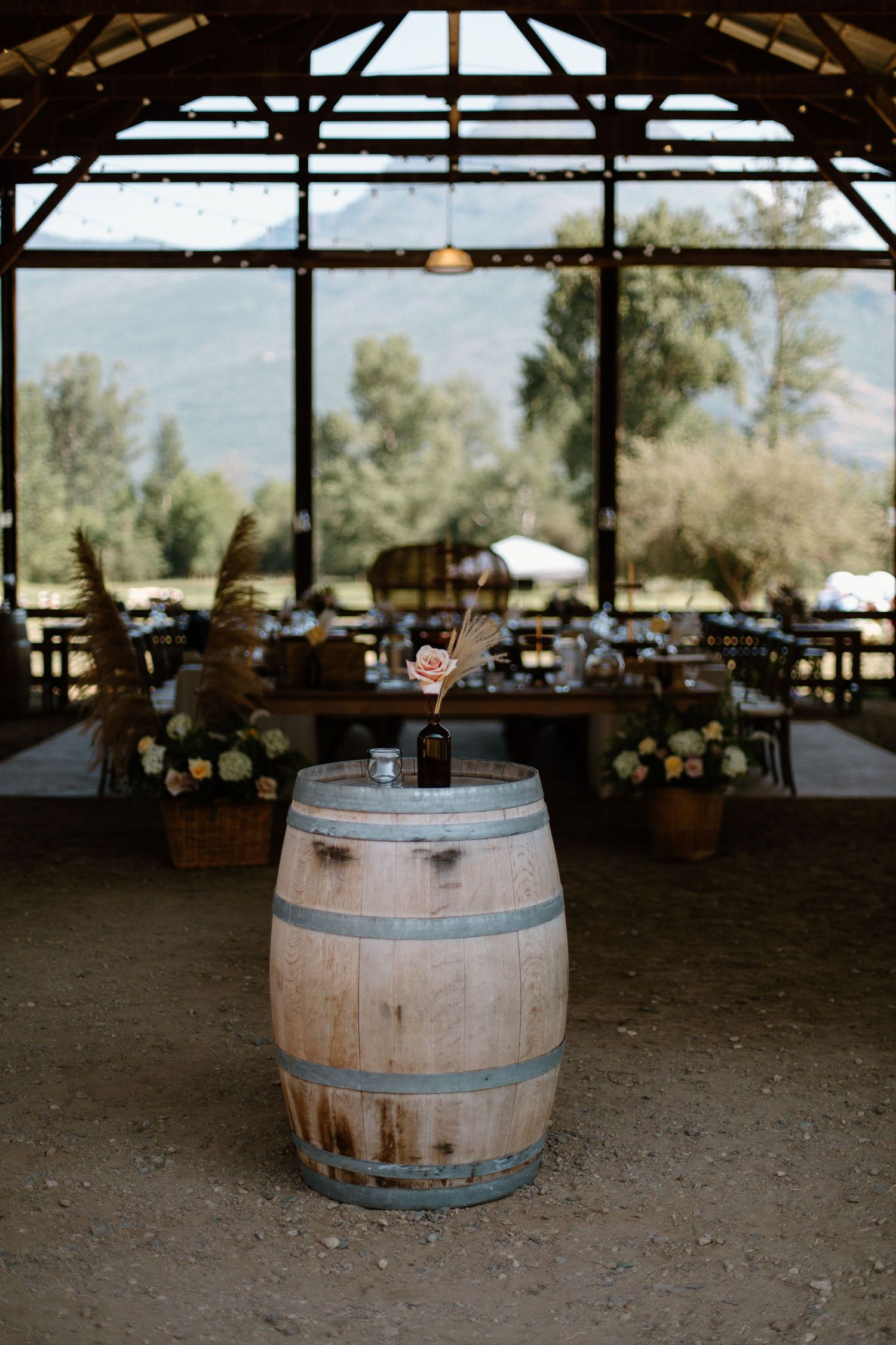 A rustic wooden wine barrel sits in an open-air venue with large windows overlooking trees and natural scenery.