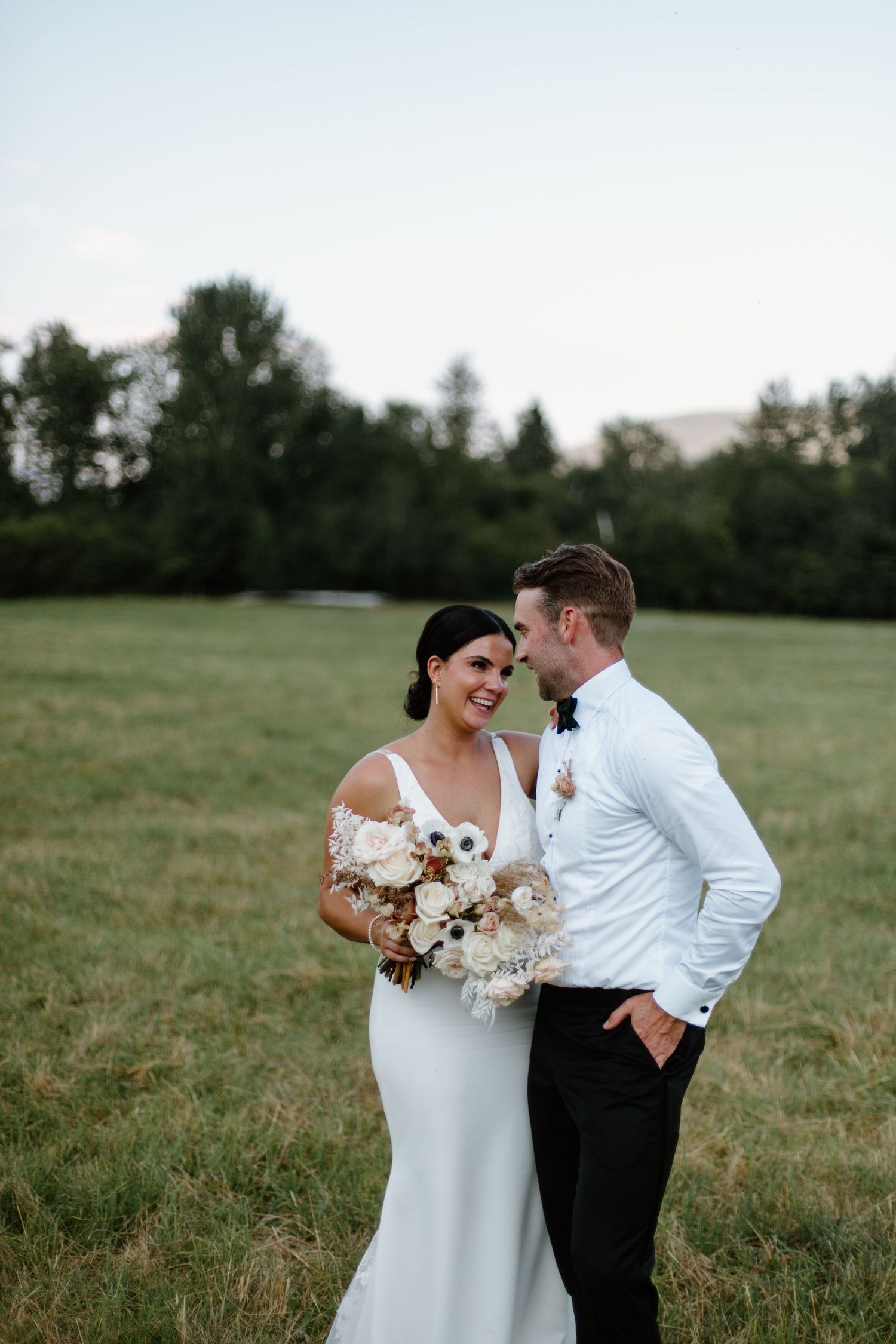 A couple shares an intimate moment in a grassy field during their wedding photoshoot.