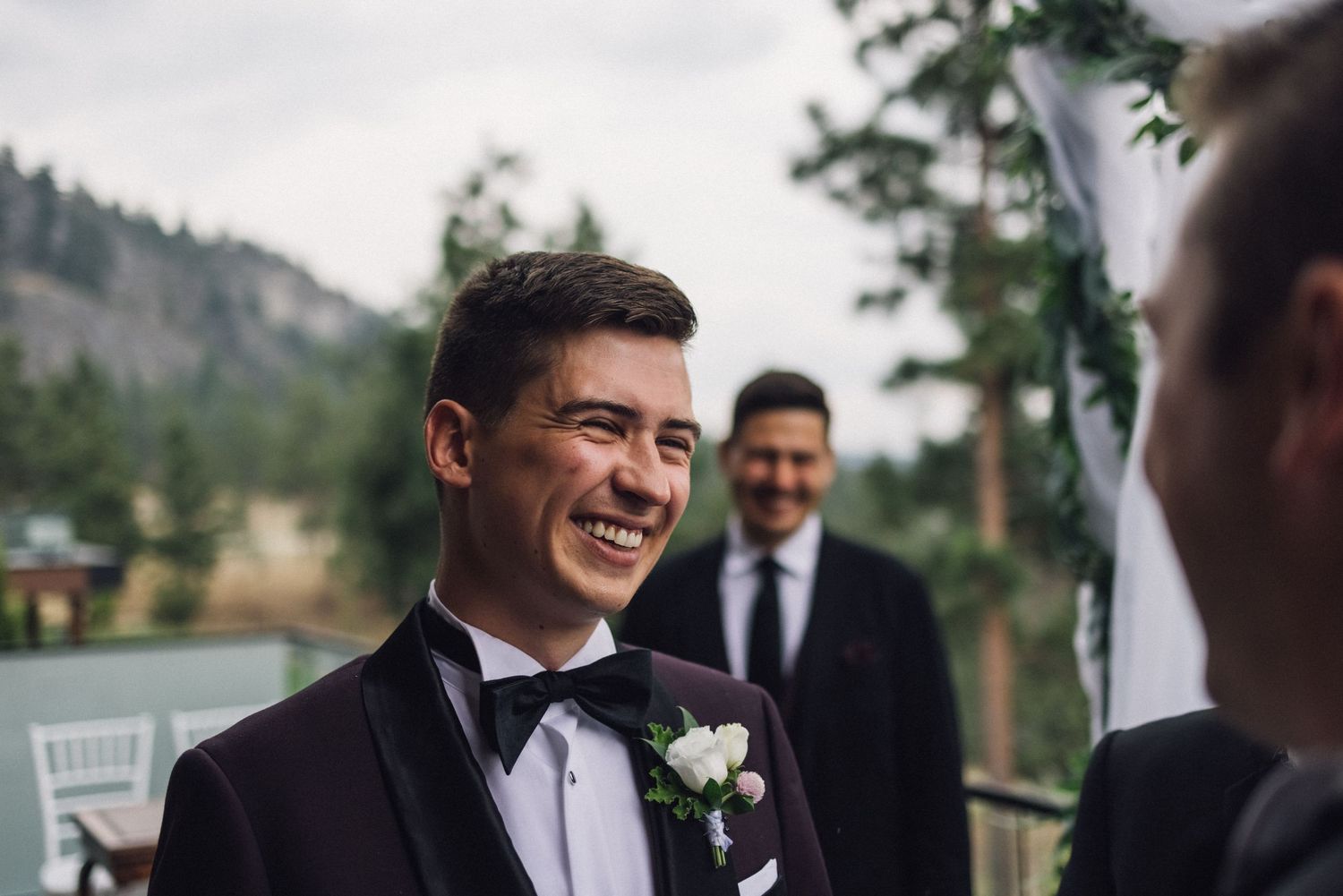 Wedding party sharing joyful moment outdoors with mountain scenery.