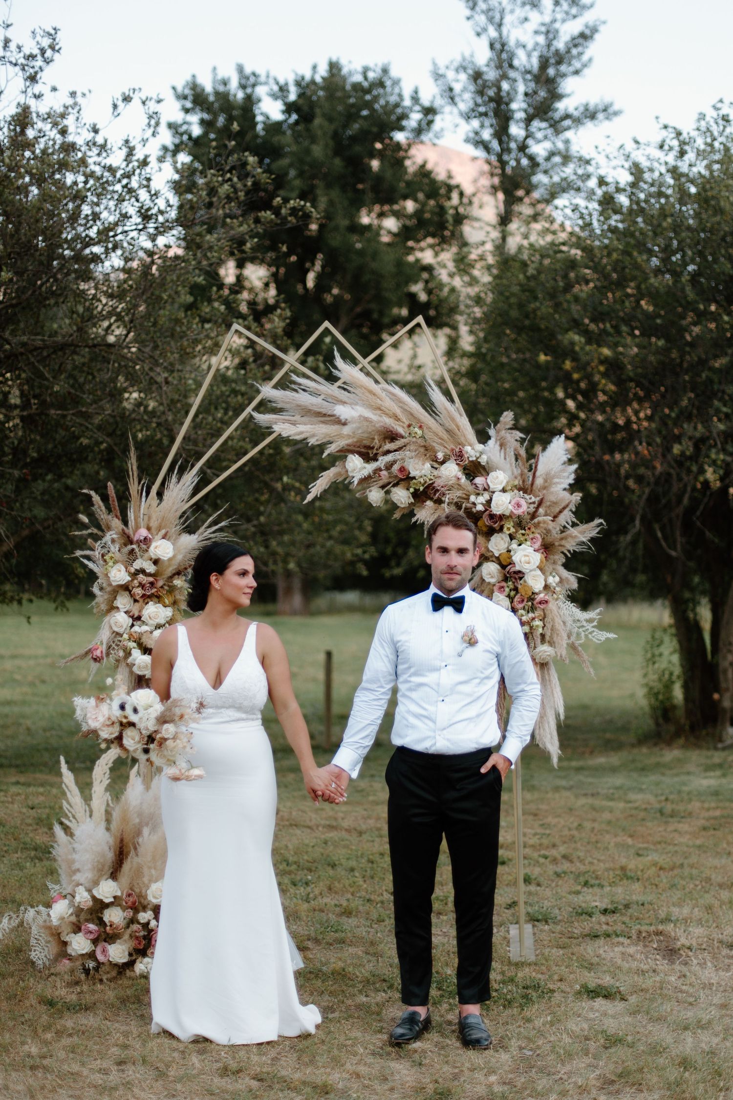 Elegant wedding ceremony setup with dried pampas grass and floral arch installation in an outdoor garden setting.