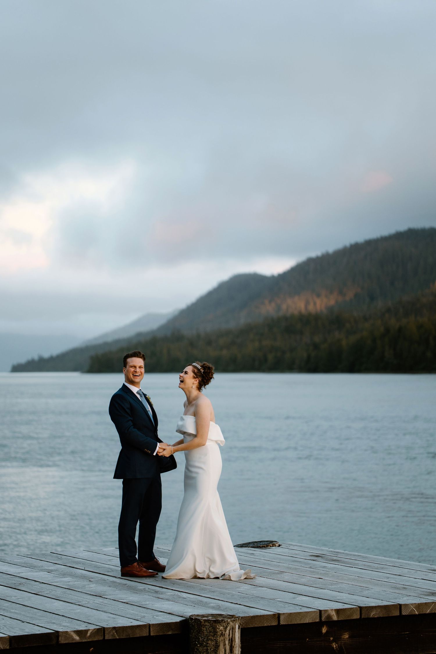 Couple sitting together on a wooden dock overlooking a misty mountain lake.