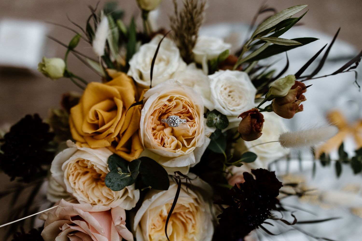 Close-up of romantic wedding bouquet with blush pink and golden yellow roses with dark greenery accents.
