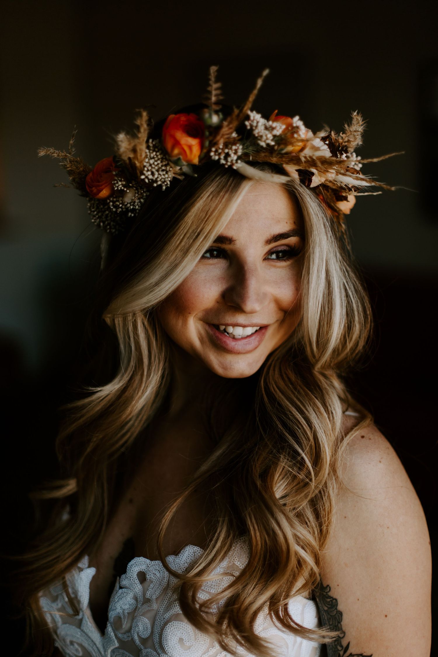 A person wearing an autumn-inspired floral crown with dried flowers and foliage against a dark moody background.