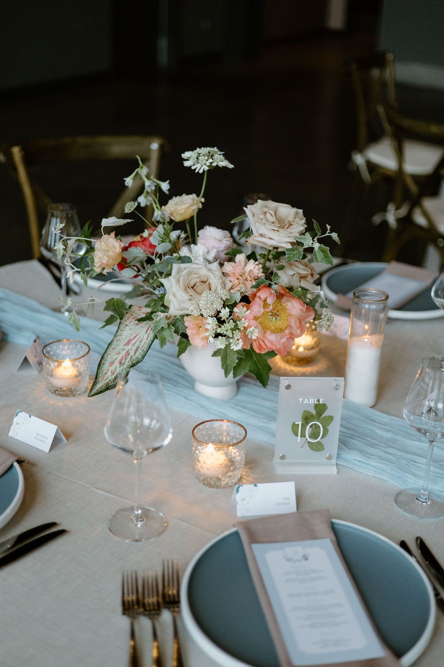 Romantic wedding reception table setting with soft pink florals, glowing candles and light blue place settings.
