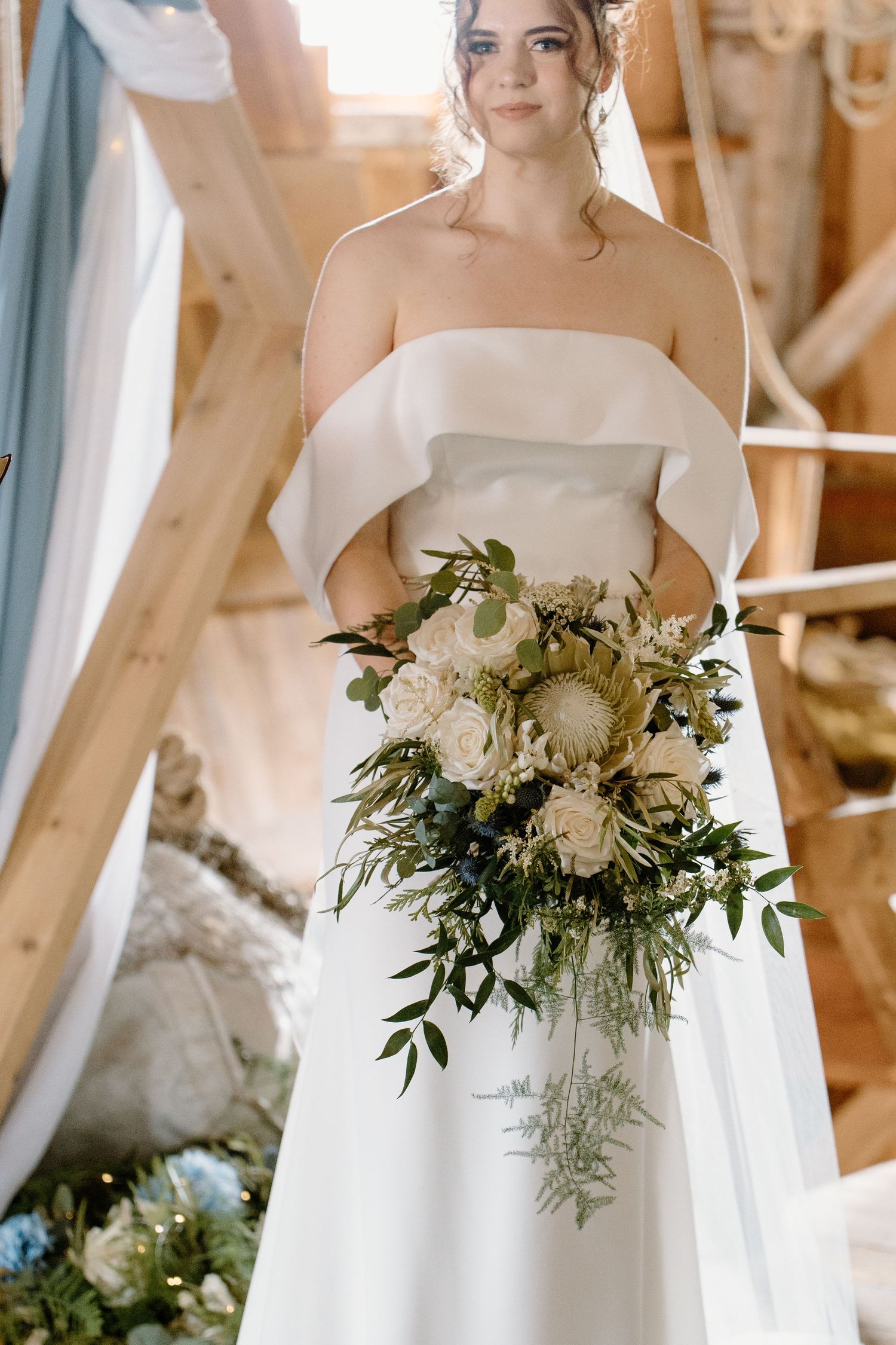 Beautiful white bridal bouquet with greenery and roses held against elegant wedding gown.