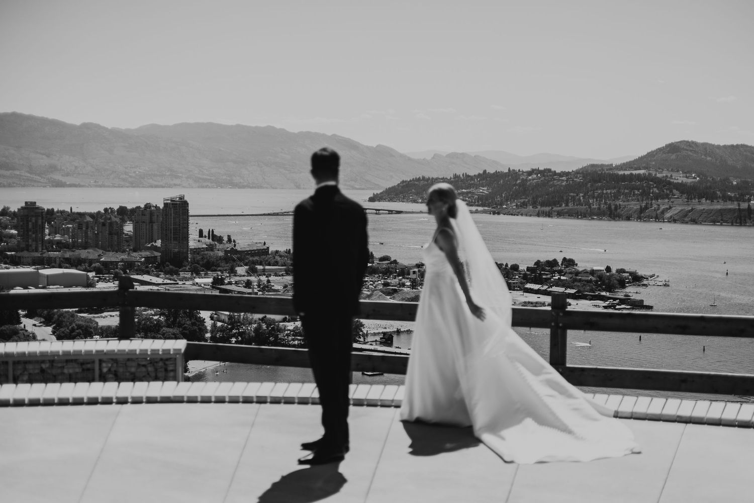 A black and white photo series showing a couple in wedding attire looking out over a harbor with boats and mountains.