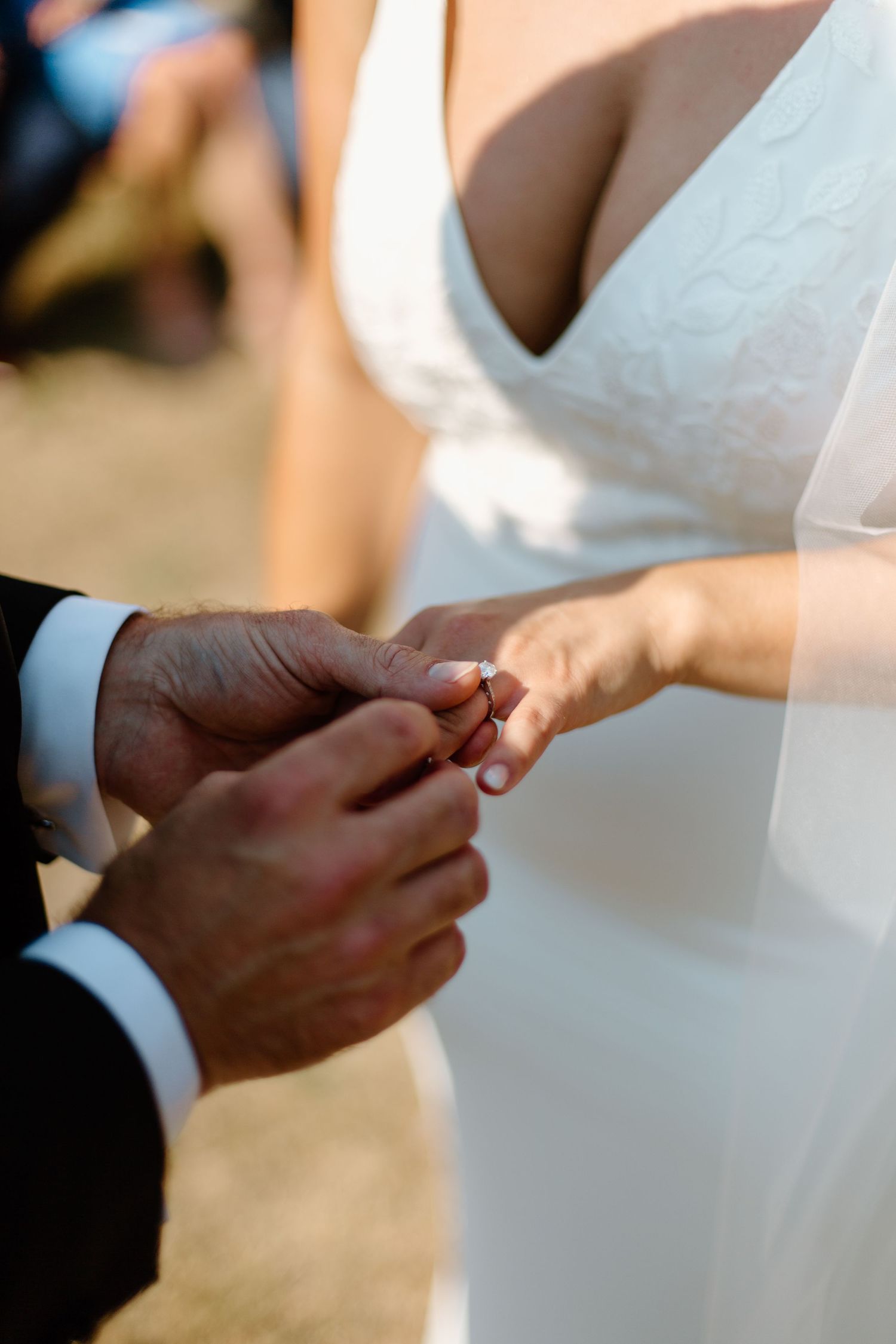 Close-up of wedding ring exchange during ceremony against white dress backdrop.