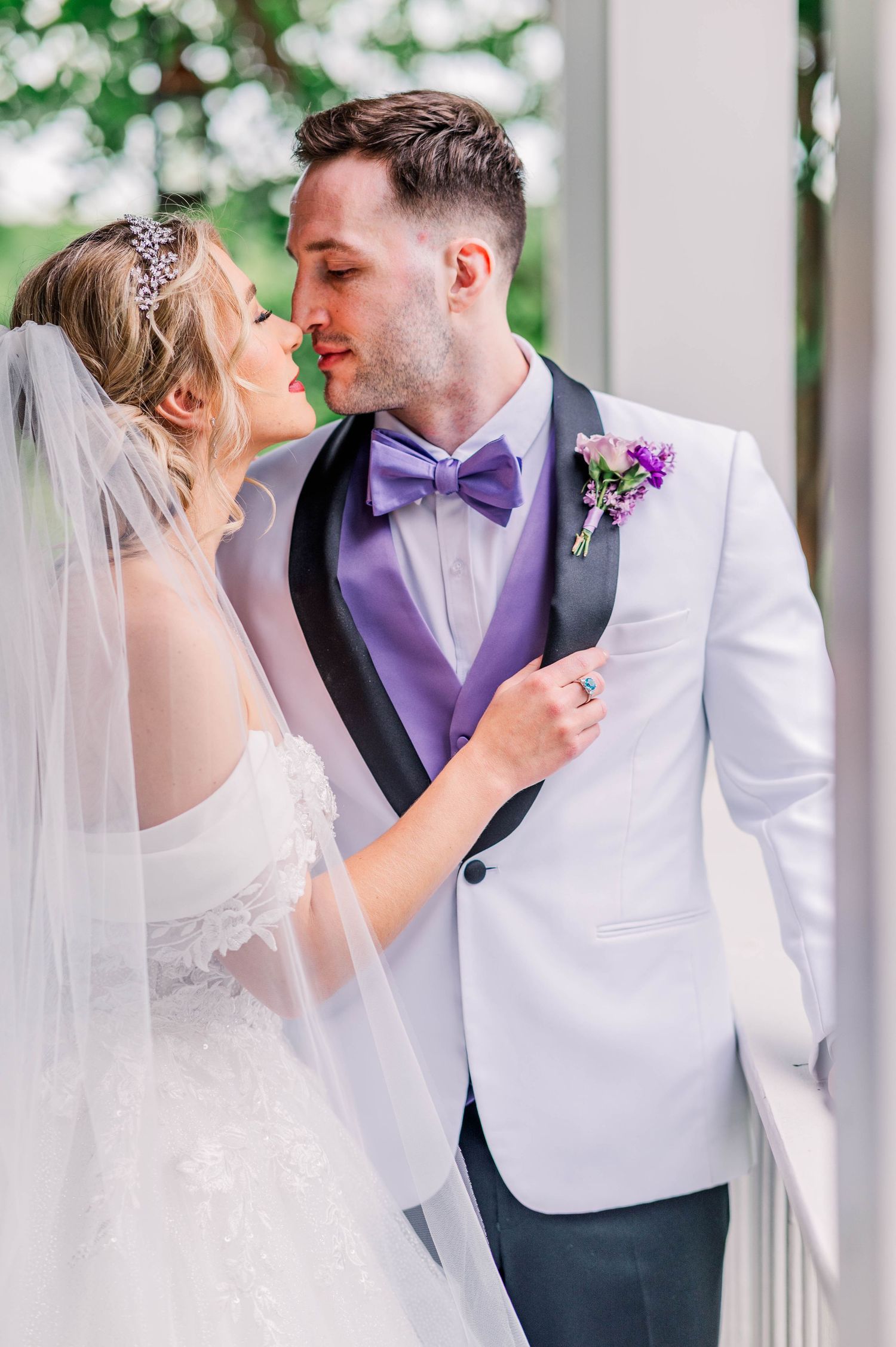 Newlywed couple sharing an intimate moment in formal attire with white tuxedo jacket and purple bow tie.