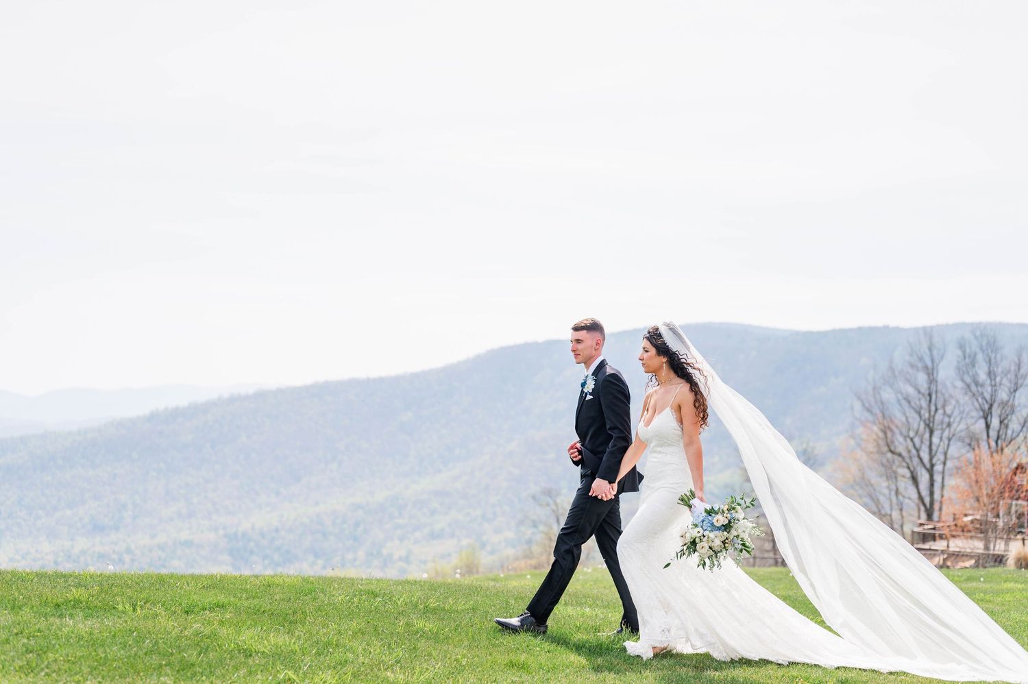 A romantic wedding couple poses in a scenic mountain landscape with a flowing veil catching the breeze.