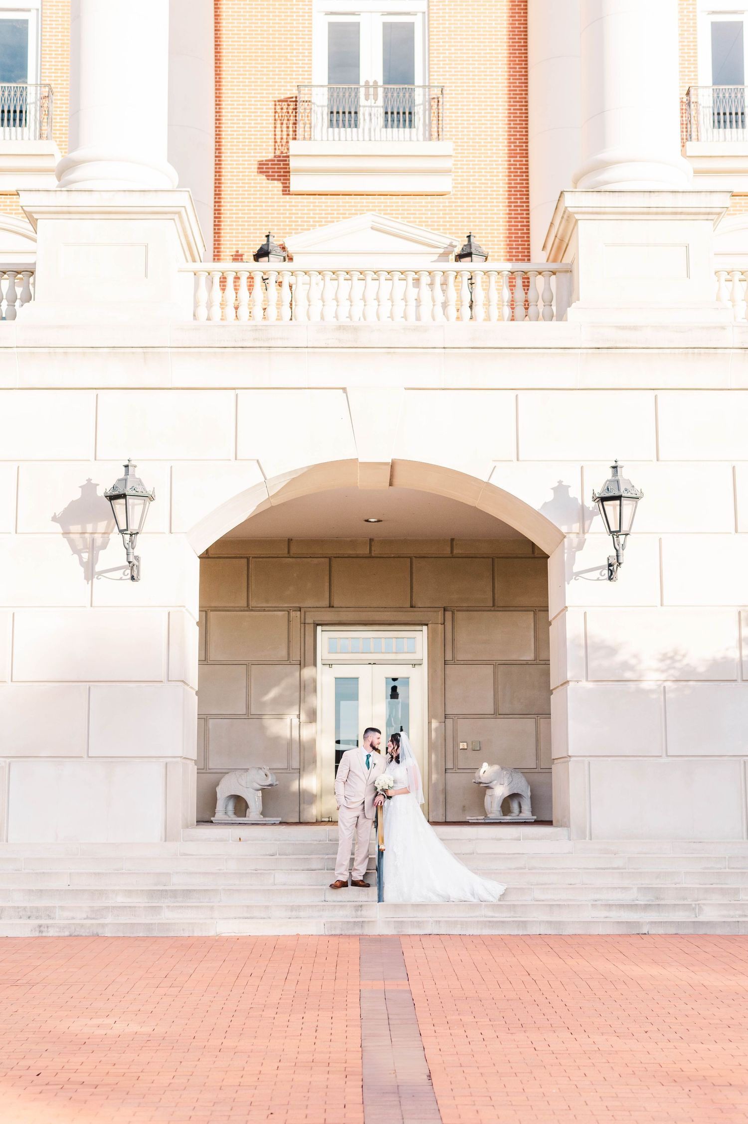 A couple poses for a wedding photo under an elegant arched entrance with white columns and lanterns at a grand hotel.