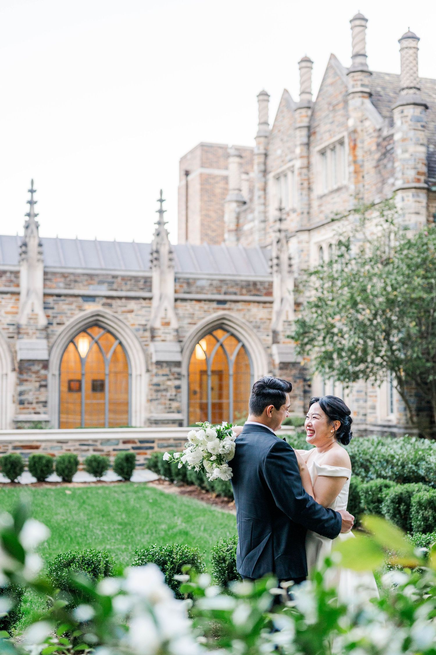 Romantic couple sharing intimate moments in front of a Gothic stone church with blooming white flowers in foreground.